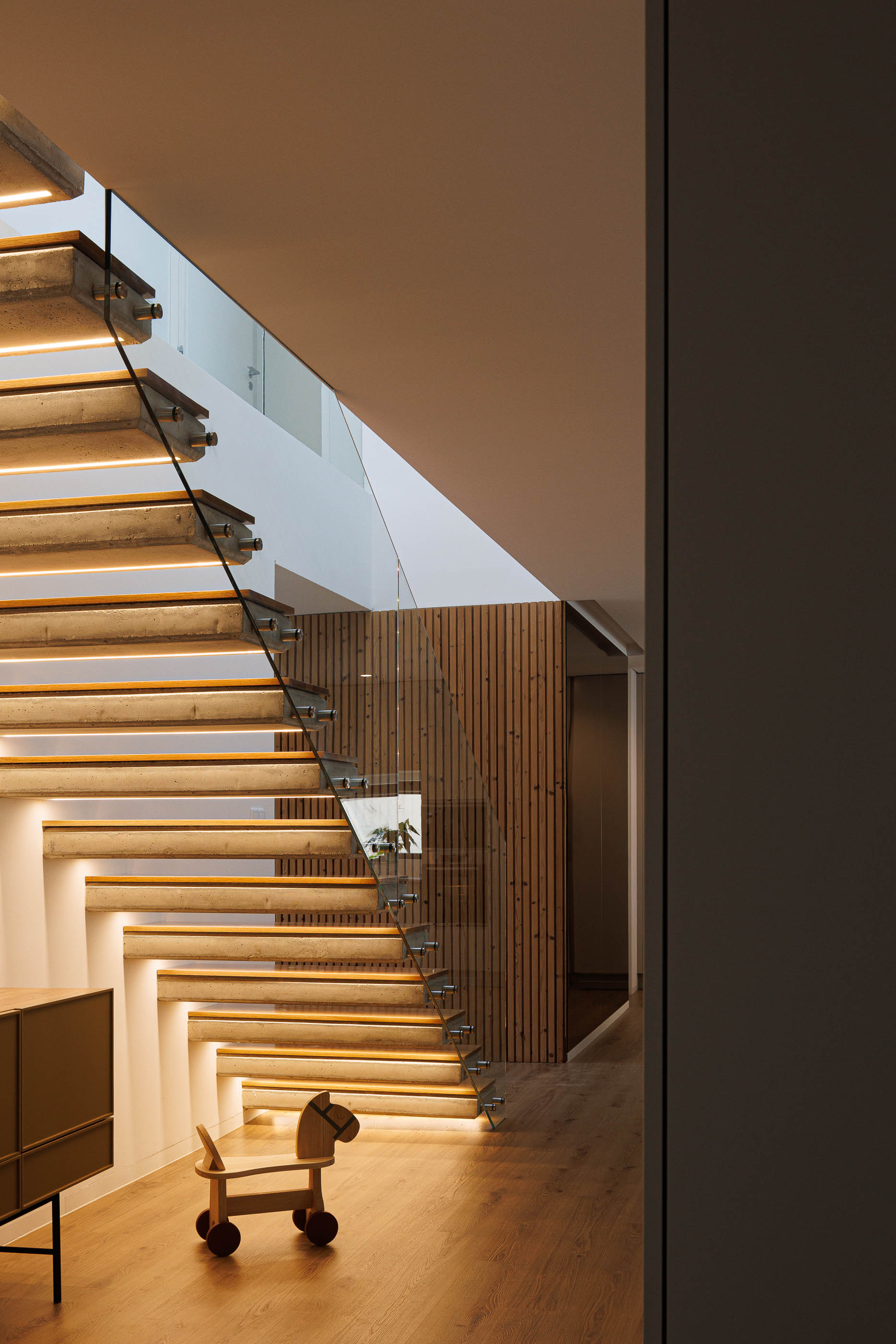 Hall: Escadas iluminadas com madeira, guarda em vidro e cavalo de madeira no pavimento. — Casa em Mundão arquitetura Um para Um, arquitectura e engenharia em Viseu