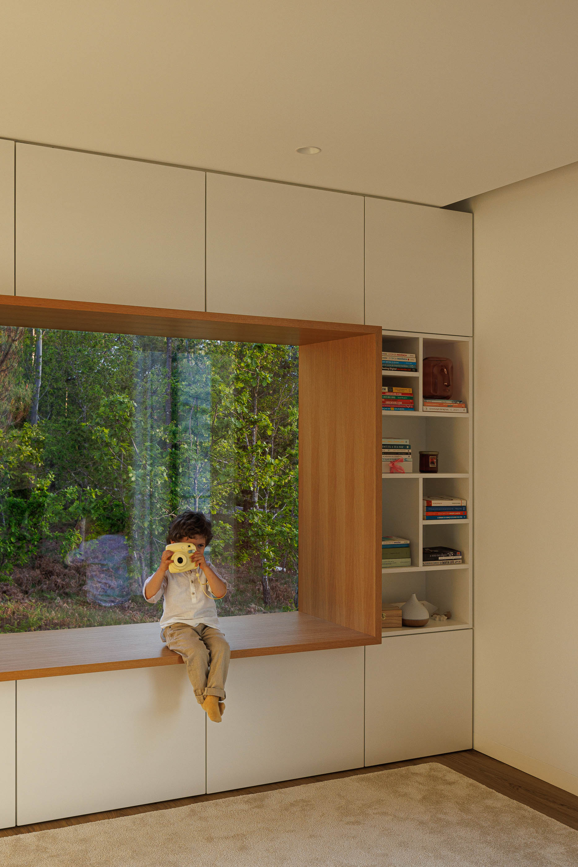 Quarto infantil: Janela embutida com vista para a floresta e criança sentada. — Casa em Mundão arquitetura Um para Um, arquitectura e engenharia em Viseu