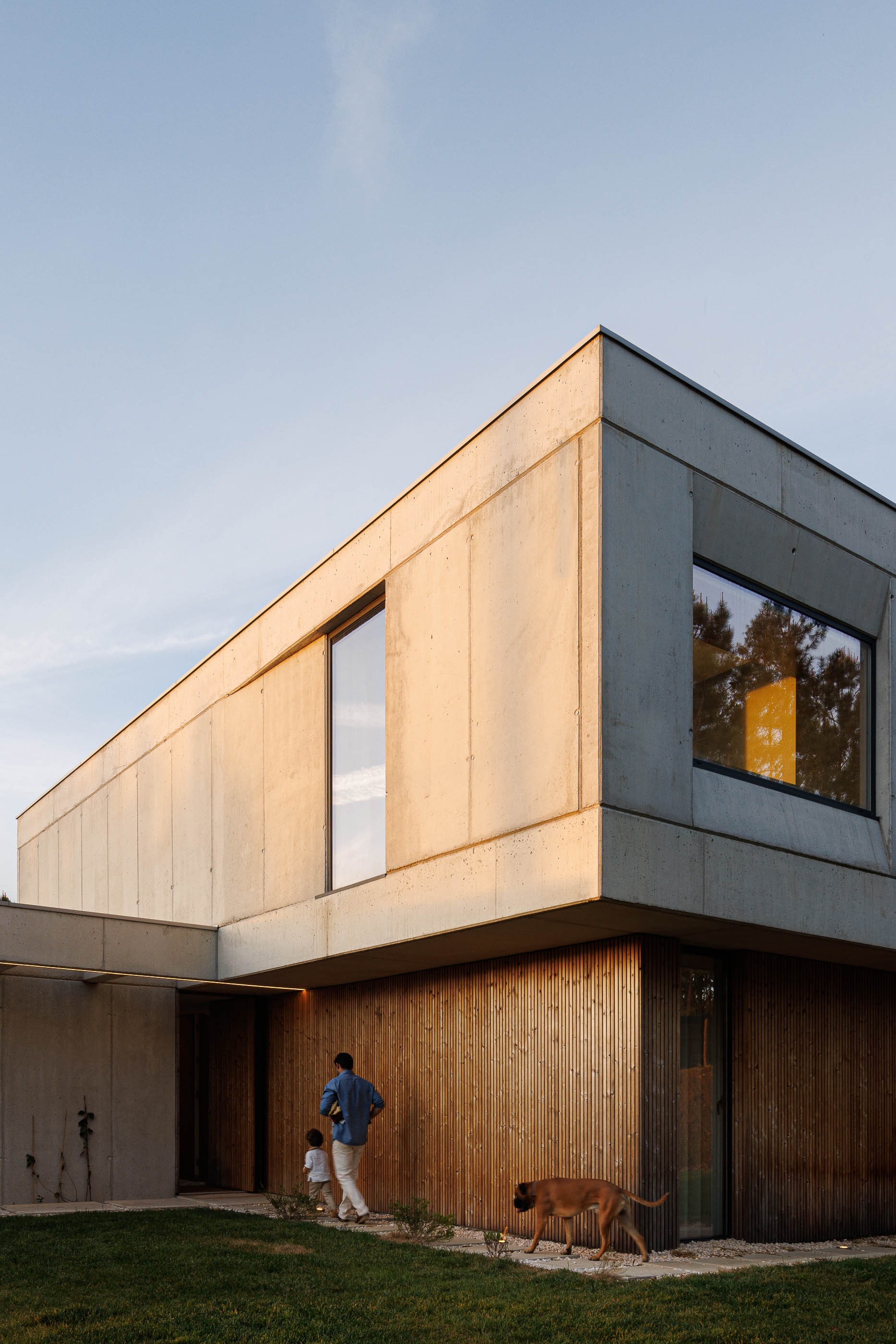 Exterior: Fachada da casa ao entardecer com detalhes em betão e madeira. — Casa em Mundão arquitetura Um para Um, arquitectura e engenharia em Viseu