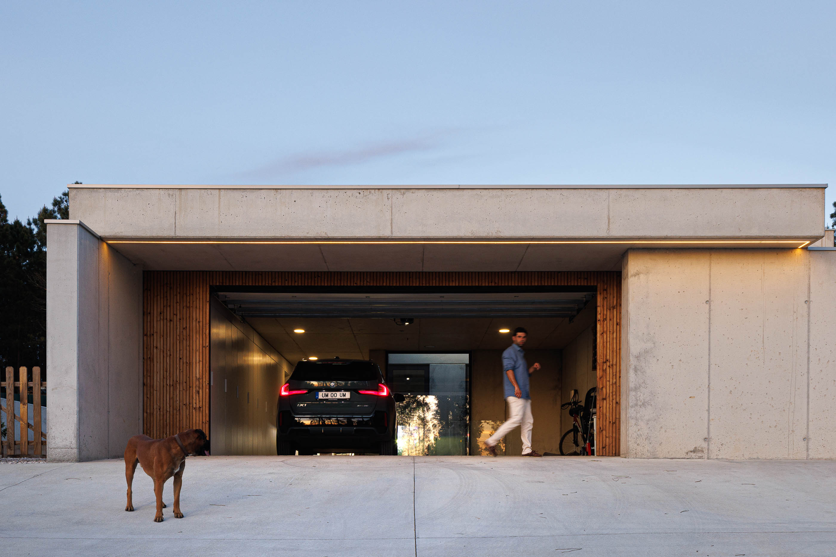 Garagem: Fachada da garagem com porta aberta, carro e pessoa a entrar. — Casa em Mundão arquitetura Um para Um, arquitectura e engenharia em Viseu
