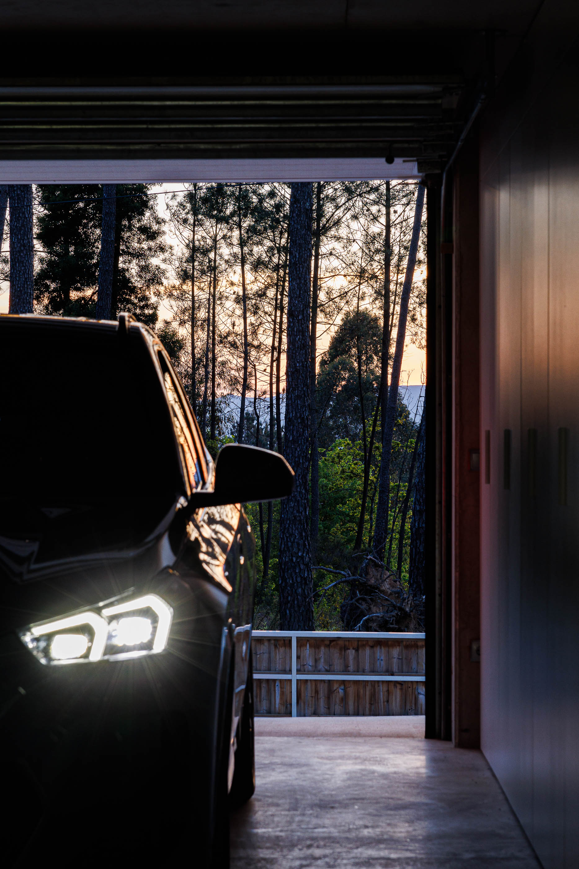 Garagem: Interior da garagem com carro e vista para a floresta ao entardecer. — Casa em Mundão arquitetura Um para Um, arquitectura e engenharia em Viseu