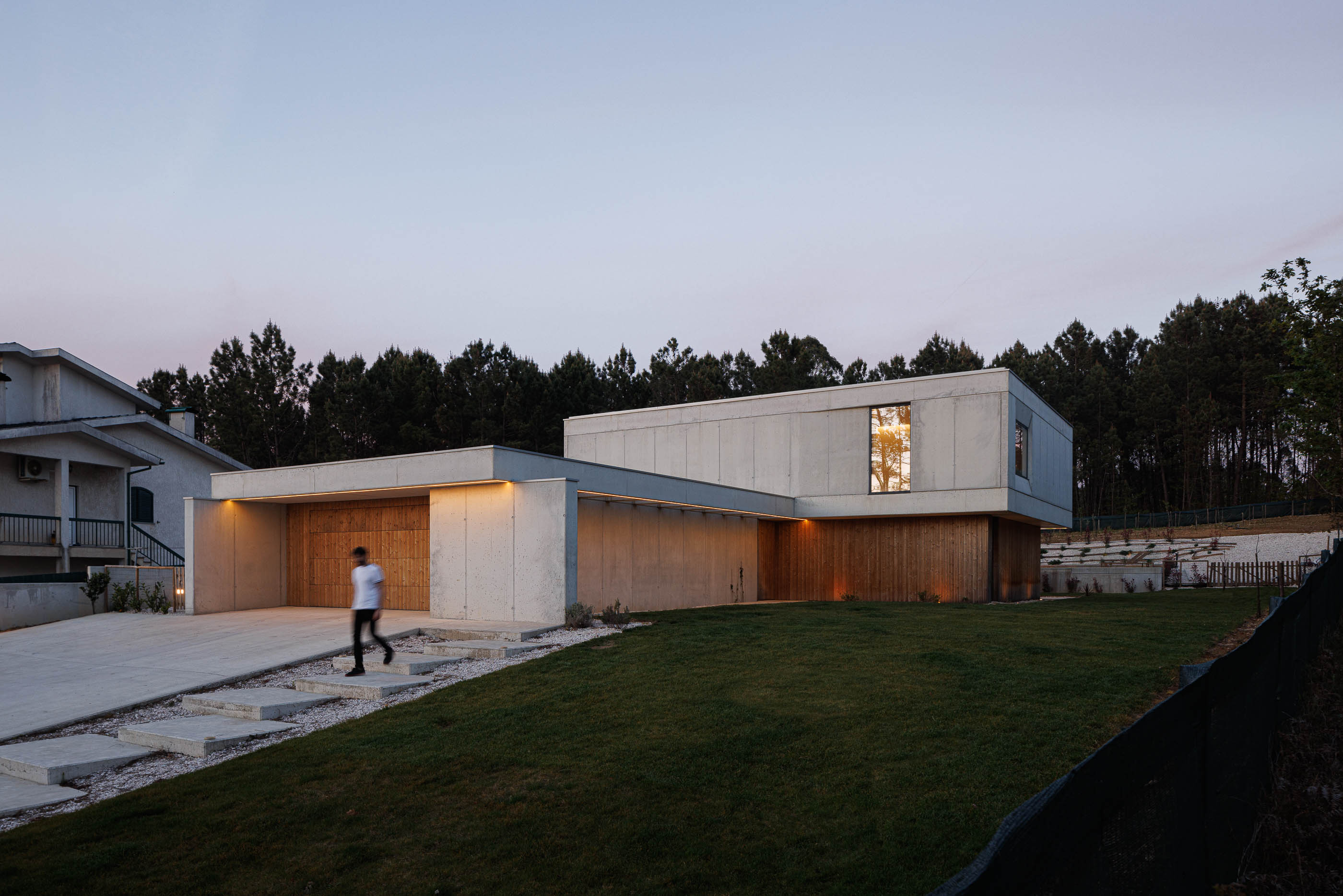Exterior: Fachada da casa ao entardecer com iluminação exterior e relvado. — Casa em Mundão arquitetura Um para Um, arquitectura e engenharia em Viseu