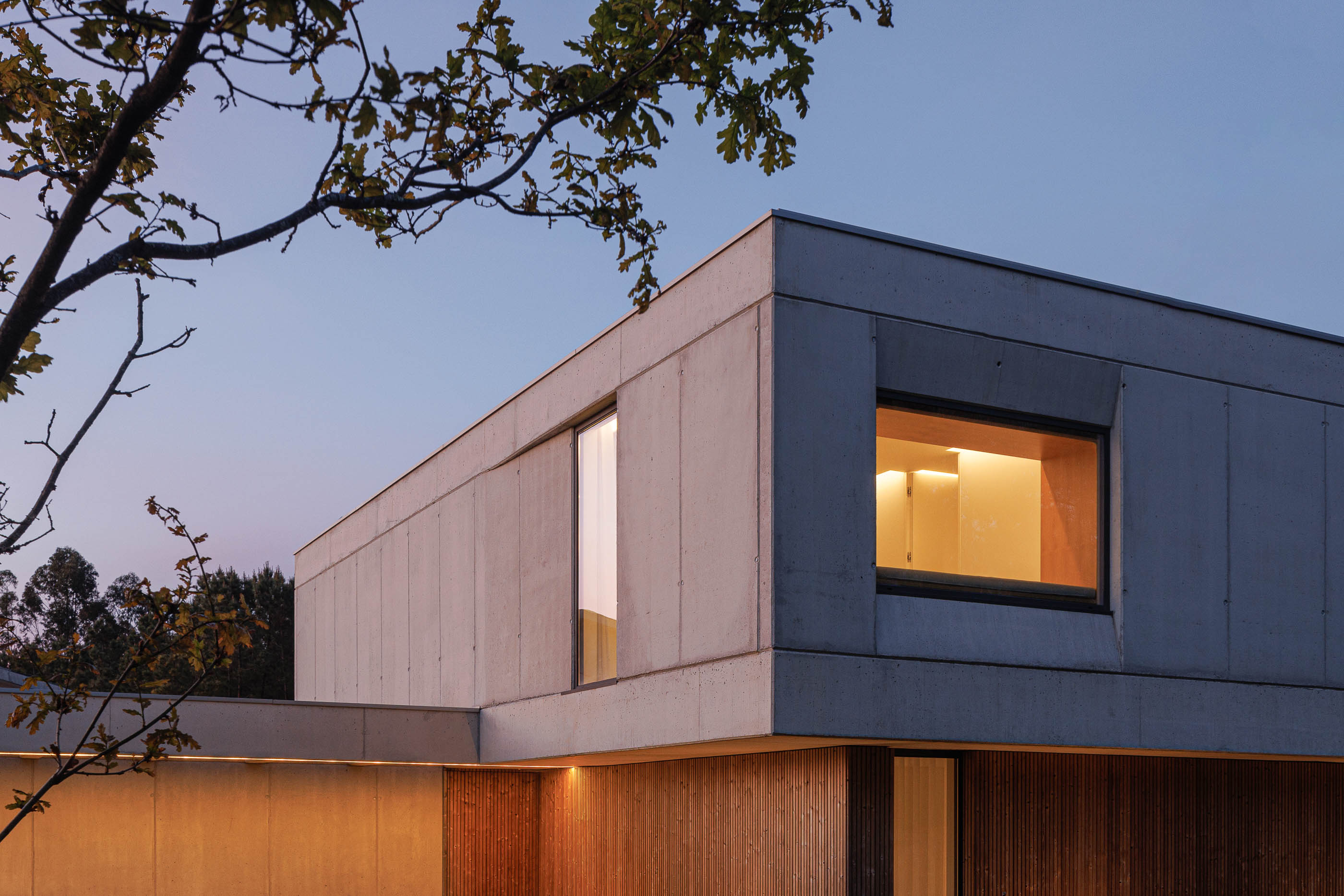Exterior: Detalhe da fachada da casa ao entardecer com janelas iluminadas. — Casa em Mundão arquitetura Um para Um, arquitectura e engenharia em Viseu