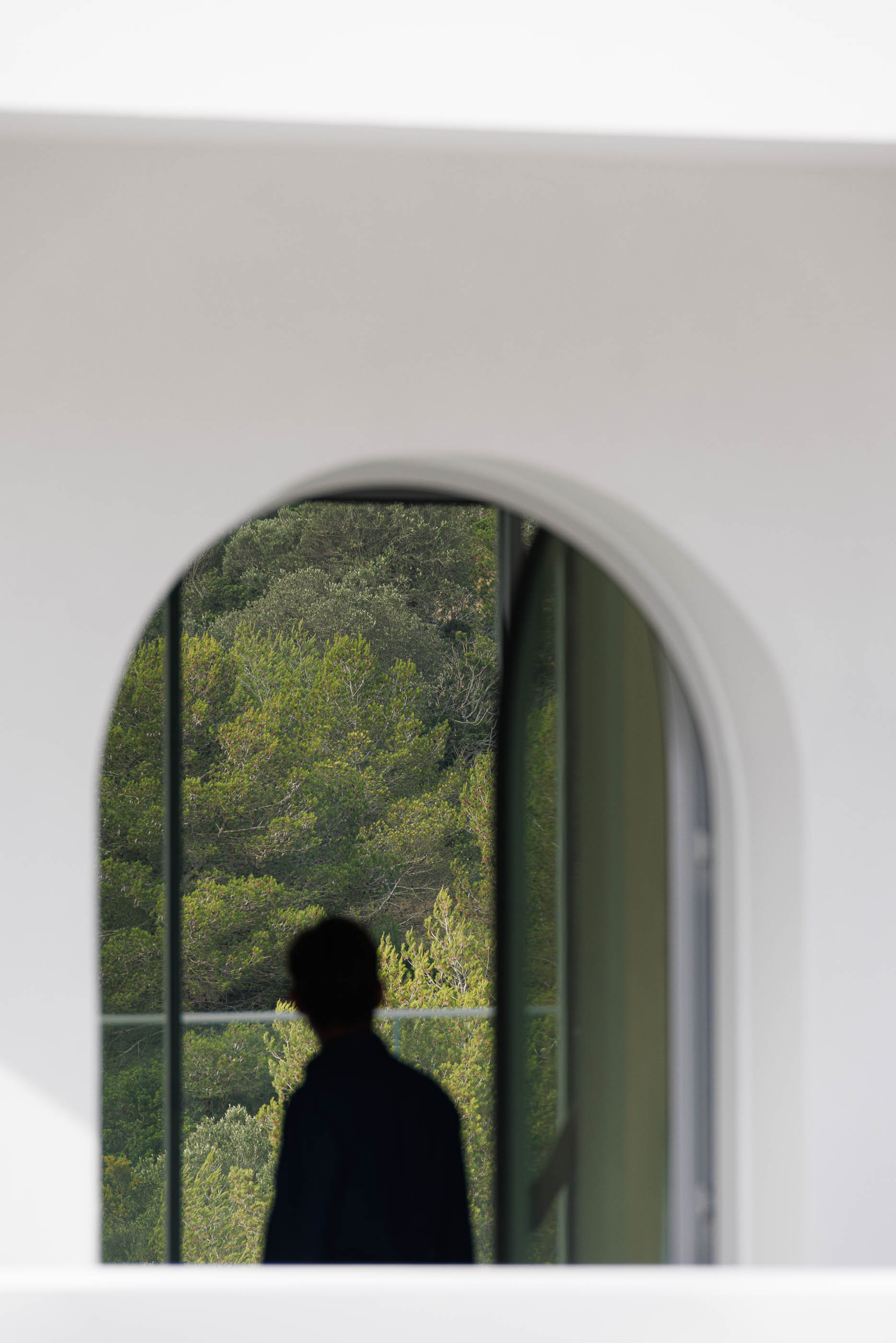 Interior: Vista em arco para a paisagem verde, silhueta de pessoa. — Villa Fortaleza arquitetura Vieira de Moura Architects em Algarve