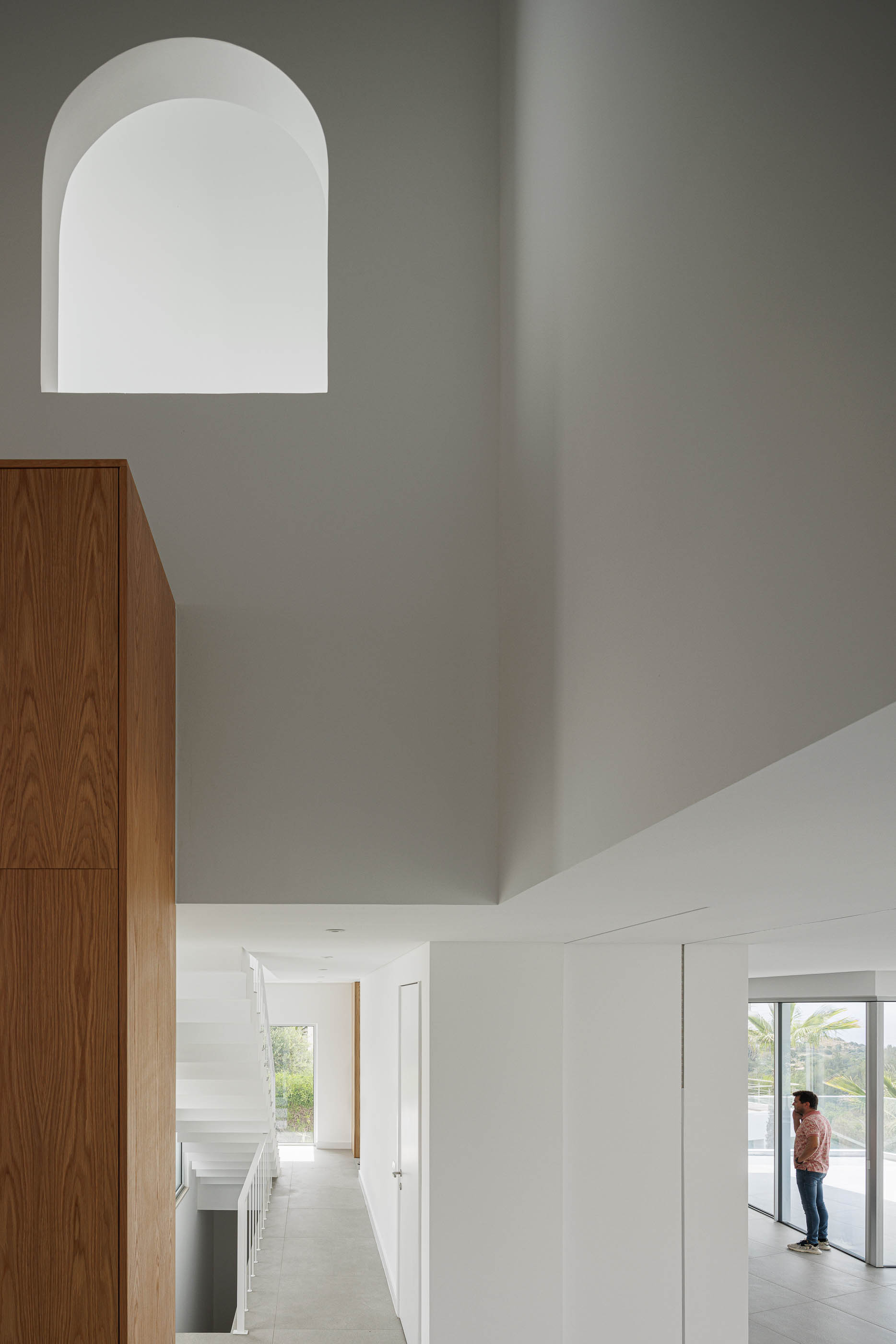 Hall de entrada: Pé direito alto, escadas brancas, armário em madeira. — Villa Fortaleza arquitetura Vieira de Moura Architects em Algarve