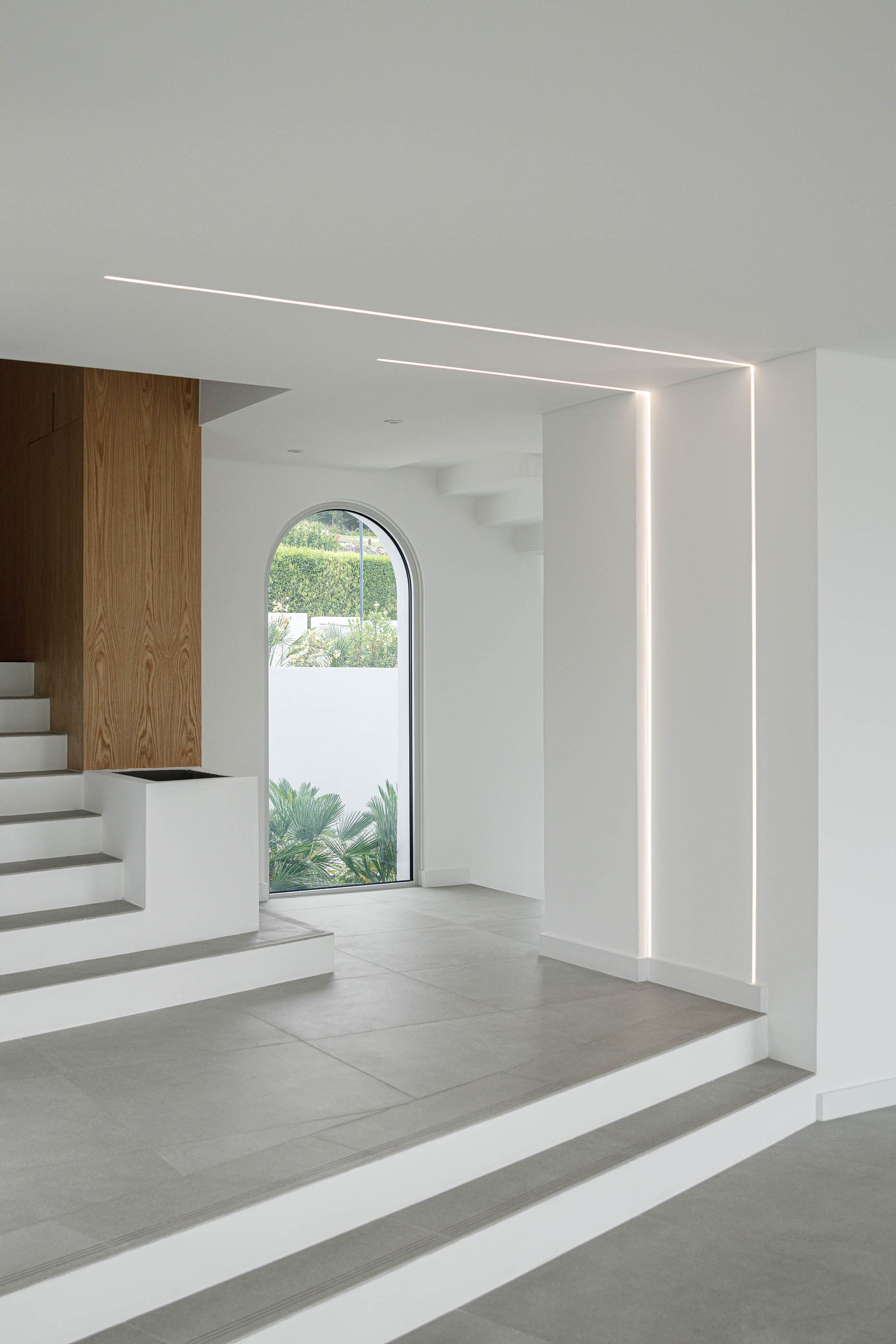 Hall de entrada: Escadas em pedra, iluminação linear, janela em arco. — Villa Fortaleza arquitetura Vieira de Moura Architects em Algarve