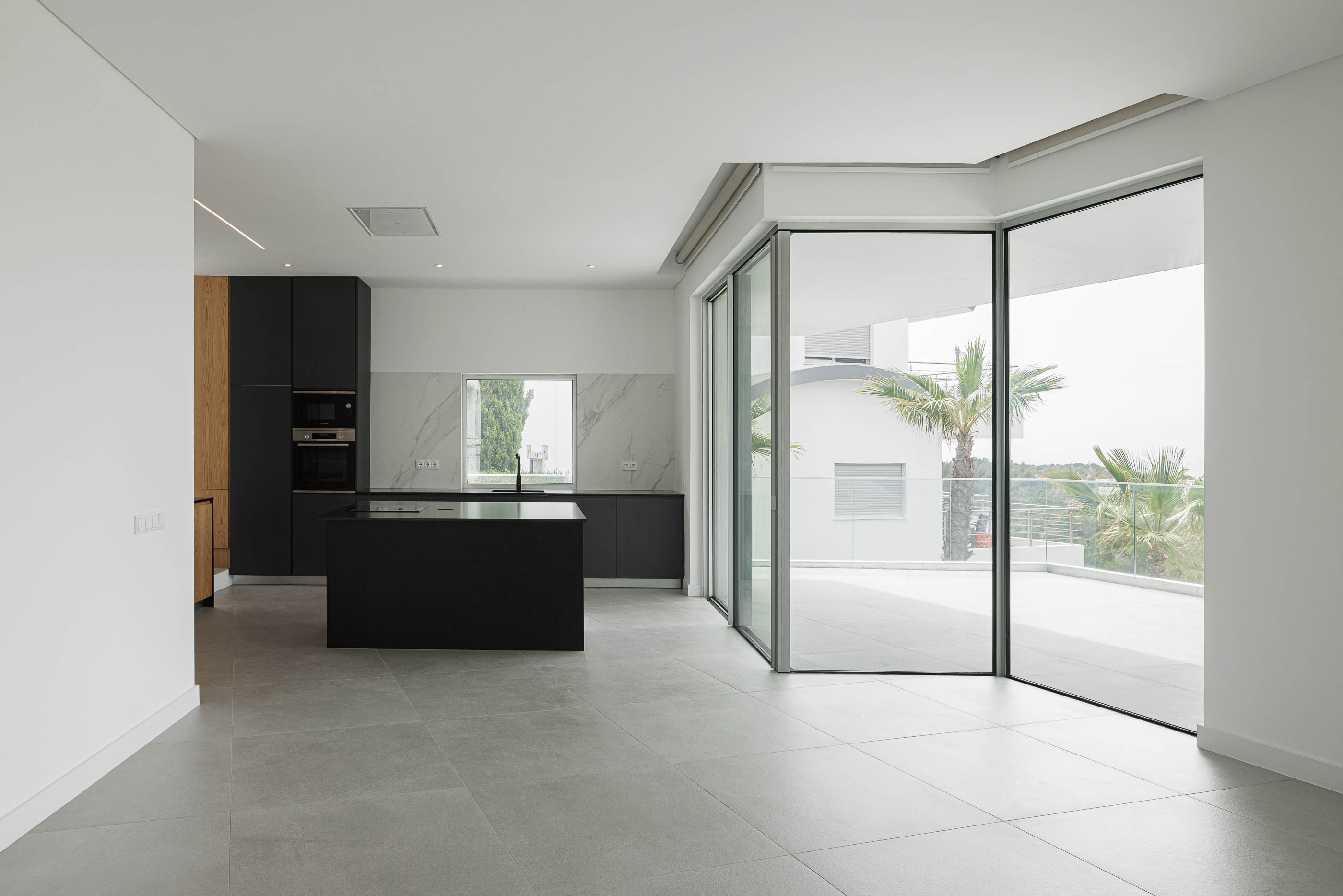 Cozinha: Espaço amplo com ilha preta, armários escuros e acesso ao terraço. — Villa Fortaleza arquitetura Vieira de Moura Architects em Algarve