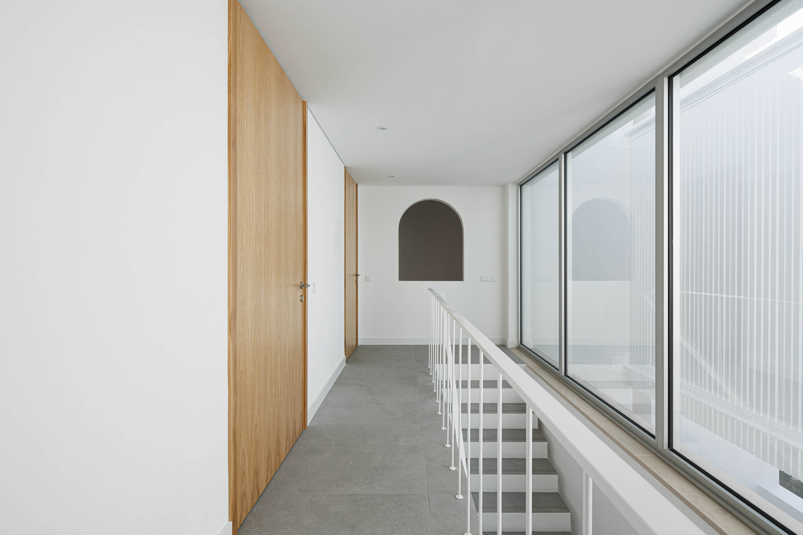 Corredor: Armários em madeira, janela em arco, escadas com corrimão branco. — Villa Fortaleza arquitetura Vieira de Moura Architects em Algarve
