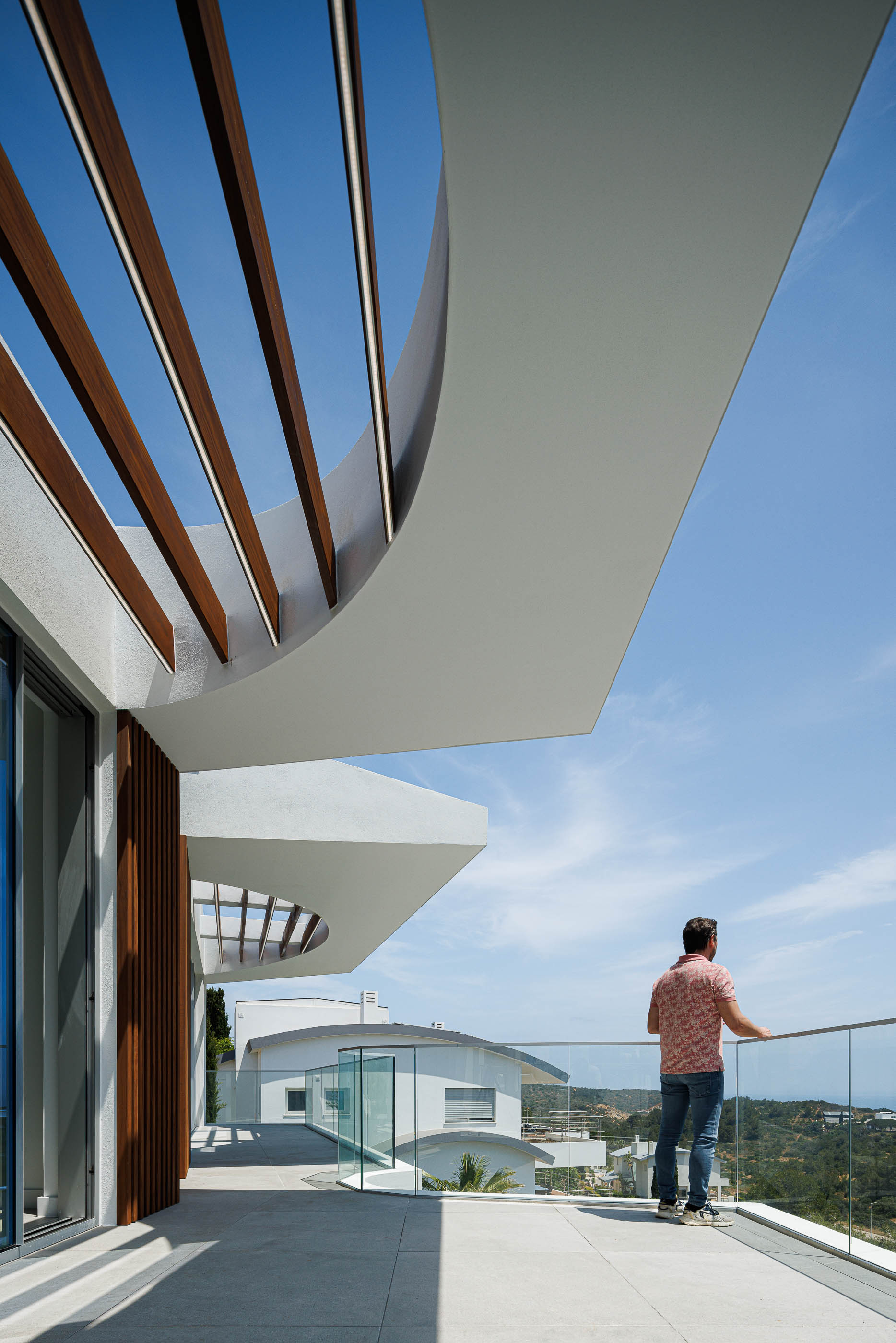 Varanda: Pessoa a apreciar a vista, pérgola em madeira e guarda em vidro. — Villa Fortaleza arquitetura Vieira de Moura Architects em Algarve