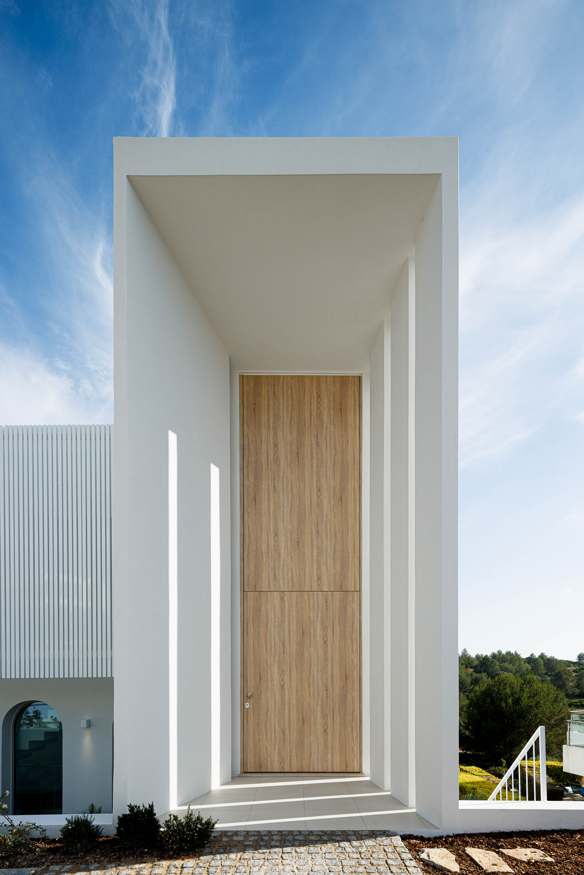 Entrada: Porta principal em madeira, enquadrada por estrutura branca alta. — Villa Fortaleza arquitetura Vieira de Moura Architects em Algarve