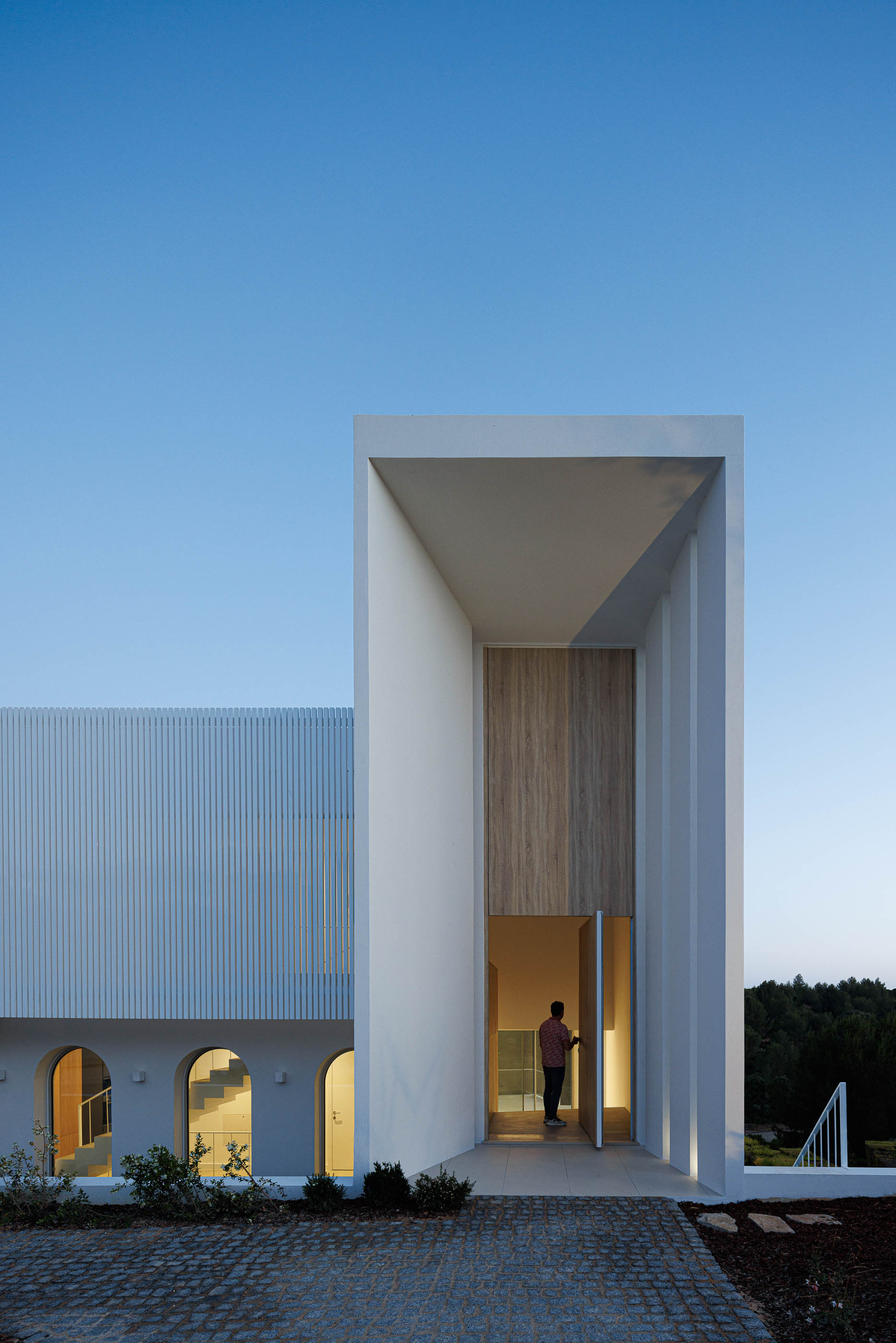 Entrada: Fachada iluminada com porta em madeira e arcos. — Villa Fortaleza arquitetura Vieira de Moura Architects em Algarve