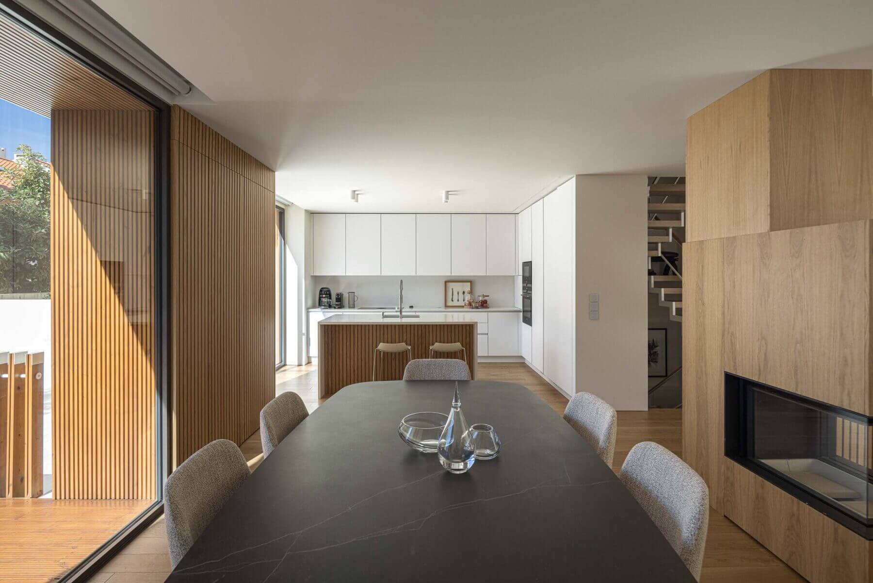 Sala de jantar: Sala de jantar com mesa preta, cadeiras cinzentas e cozinha aberta, com lareira em madeira. — Casa Forca-Vouga arquitetura RVDM - Ricardo Vieira de Melo, arquitectos em Aveiro