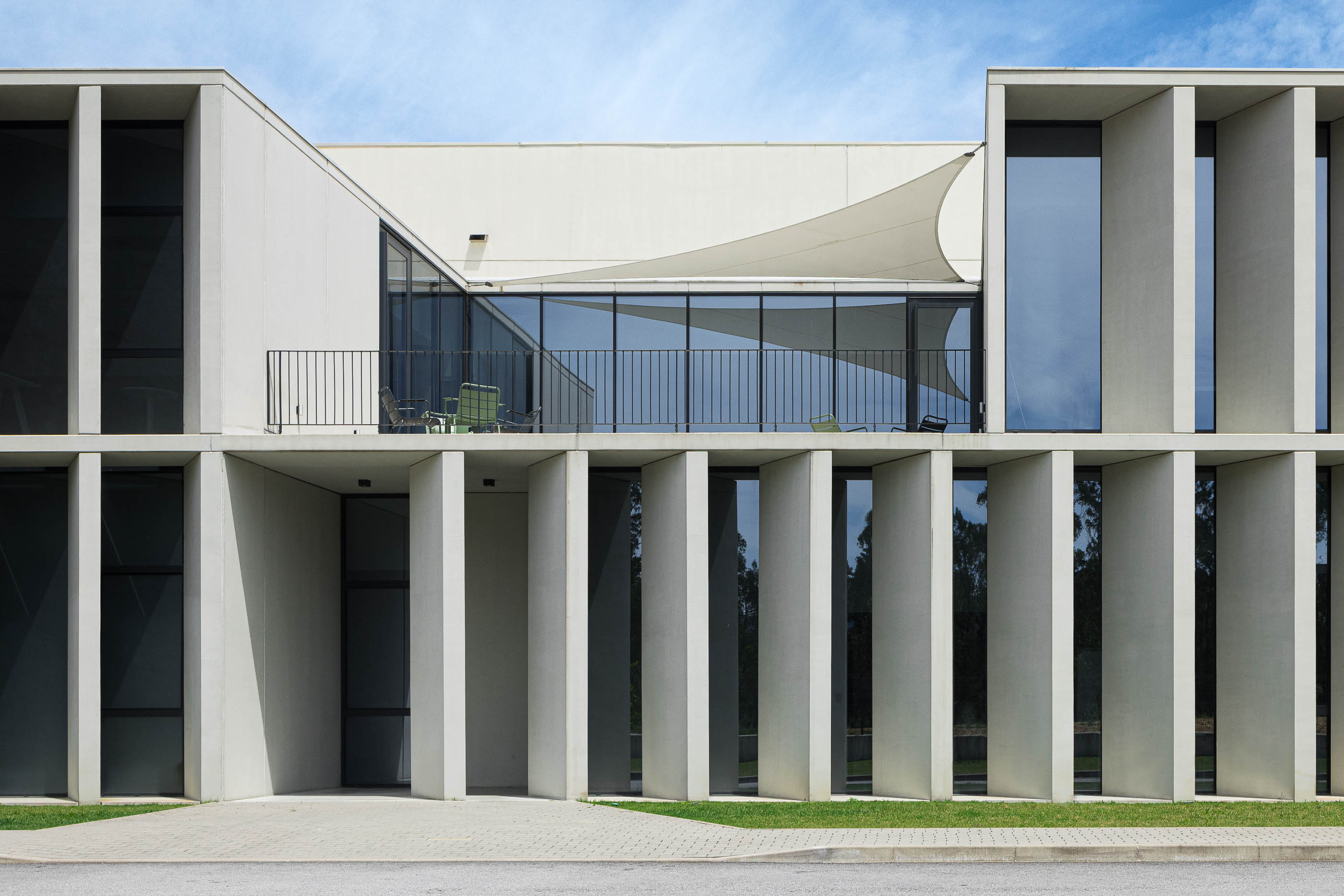 Fachada: Edifício industrial com colunas de betão branco, janelas envidraçadas e varanda com toldo. — BW II – Edifício Industrial em Viana do Castelo arquitetura Multiprojectus em Viana do Castelo