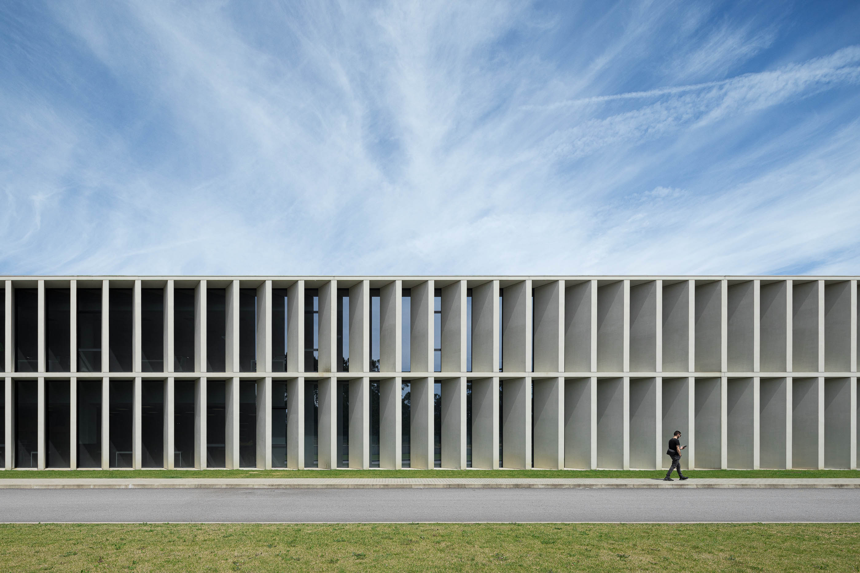 Exterior: Longa fachada do edifício com colunas de betão, janelas e pessoa a caminhar. — BW II – Edifício Industrial em Viana do Castelo arquitetura Multiprojectus em Viana do Castelo