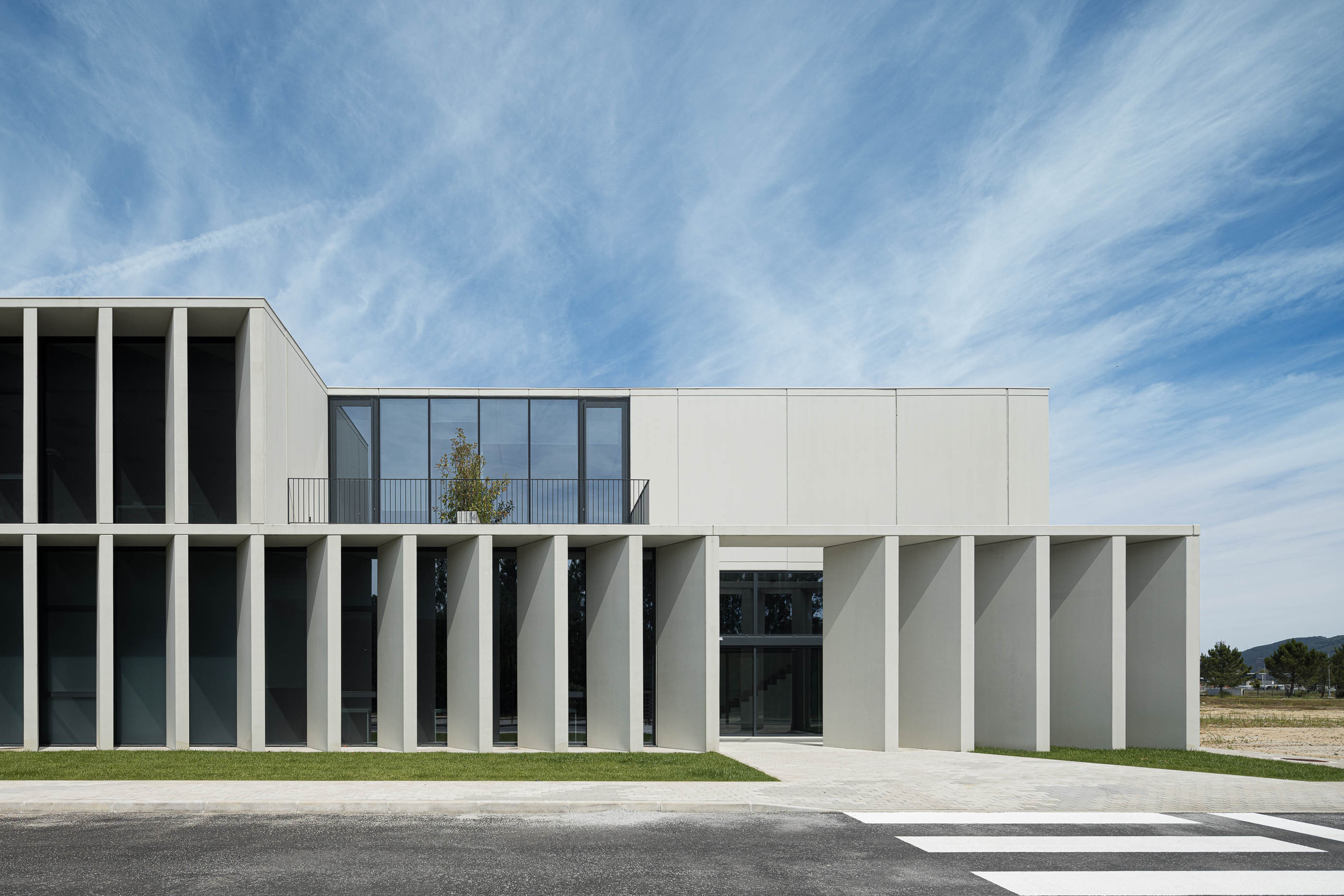 Exterior: Edifício com fachada em betão branco, colunas verticais e varanda com vegetação. — BW II – Edifício Industrial em Viana do Castelo arquitetura Multiprojectus em Viana do Castelo