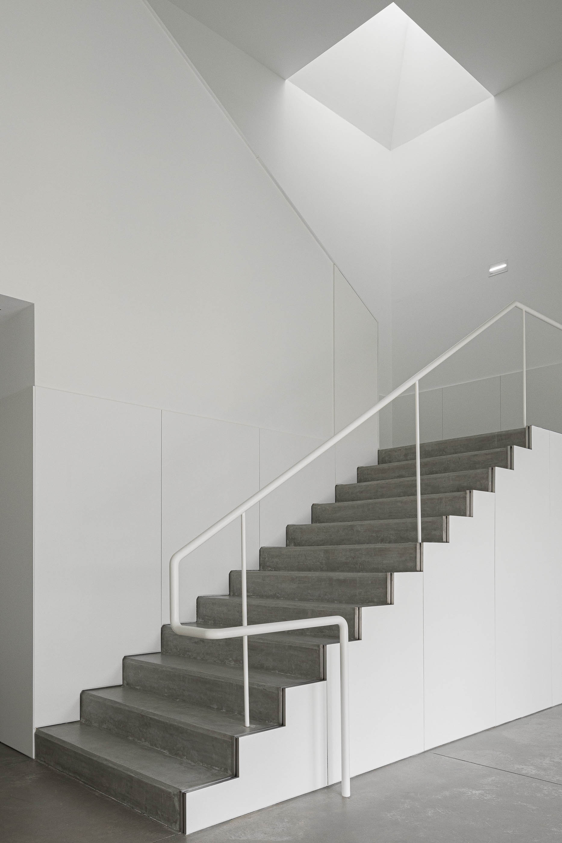 Escadaria: Escadas em betão com corrimão branco, iluminação zenital e paredes brancas. — BW II – Edifício Industrial em Viana do Castelo arquitetura Multiprojectus em Viana do Castelo
