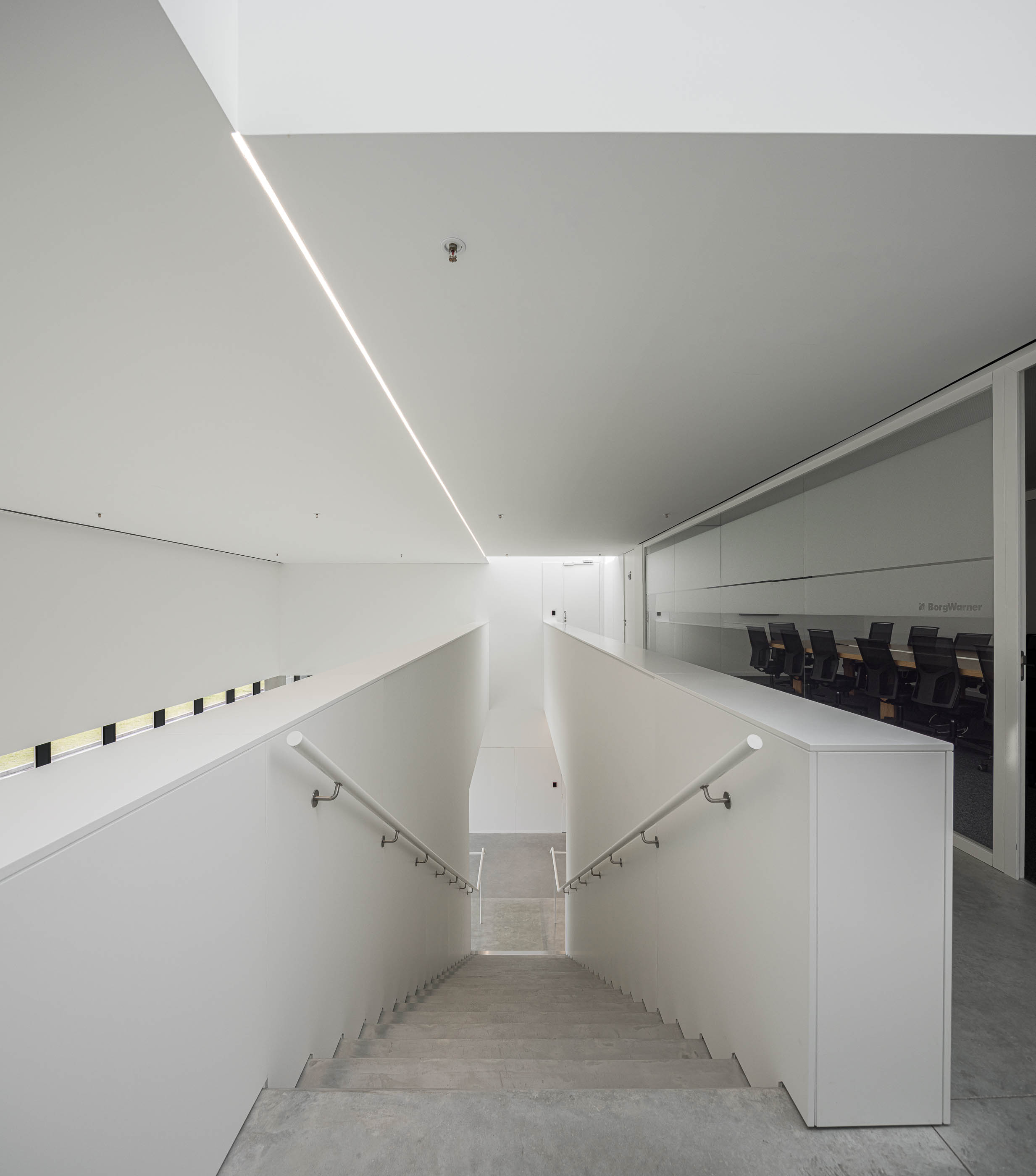 Escadaria: Vista do topo da escadaria com corrimão branco, paredes brancas e luz linear. — BW II – Edifício Industrial em Viana do Castelo arquitetura Multiprojectus em Viana do Castelo