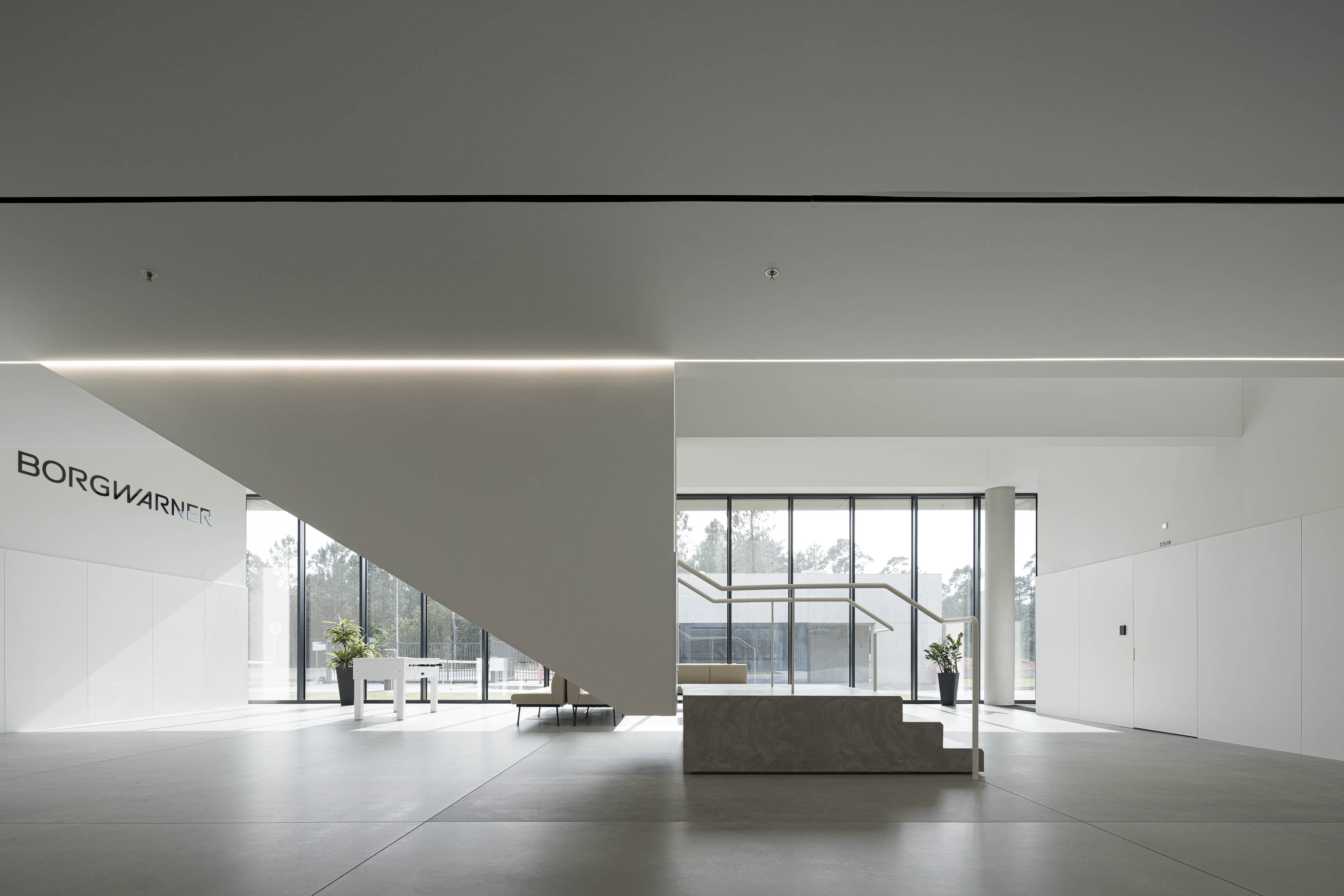 Escadaria: Hall de entrada com escadas em betão, corrimão branco e zona de estar. — BW II – Edifício Industrial em Viana do Castelo arquitetura Multiprojectus em Viana do Castelo