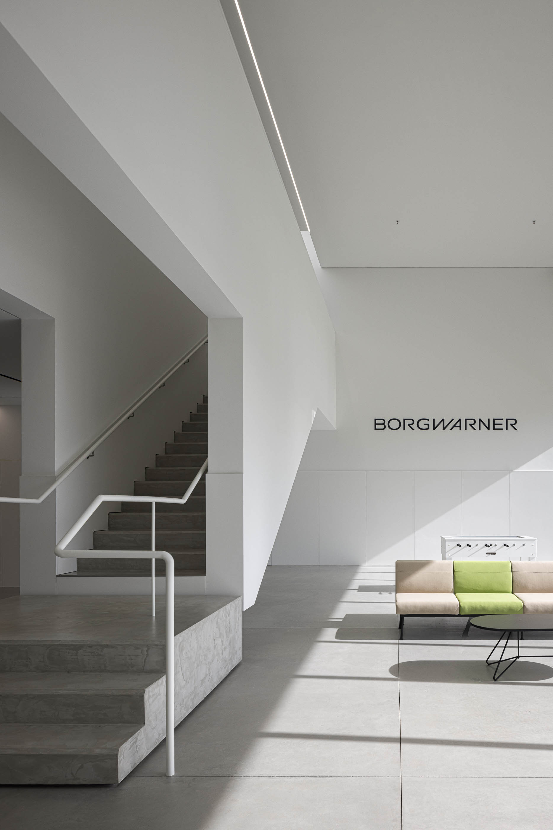 Escadaria: Hall de entrada com escadas em betão, corrimão branco e sofás modernos. — BW II – Edifício Industrial em Viana do Castelo arquitetura Multiprojectus em Viana do Castelo