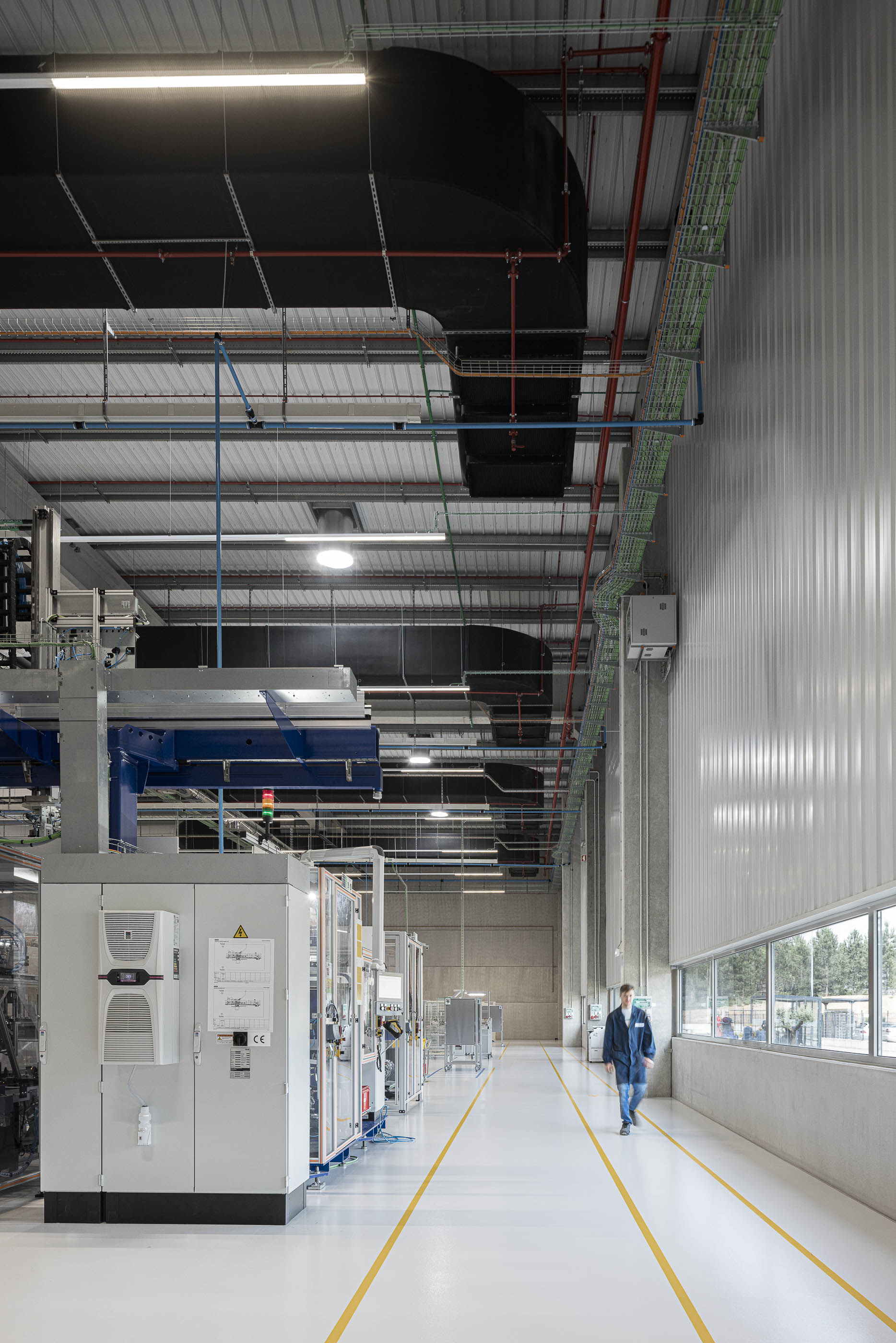 Escritório: Espaço de trabalho amplo com secretárias, cadeiras pretas e divisórias em vidro. — BW II – Edifício Industrial em Viana do Castelo arquitetura Multiprojectus em Viana do Castelo