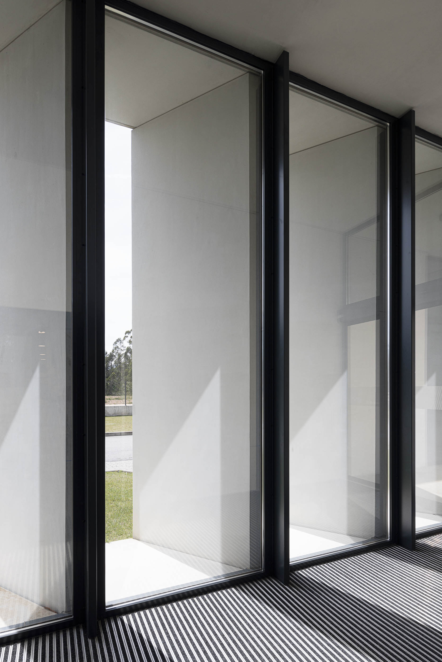 Refeitório: Sala de refeições com mesas, cadeiras pretas e janelas amplas com cortinas. — BW II – Edifício Industrial em Viana do Castelo arquitetura Multiprojectus em Viana do Castelo