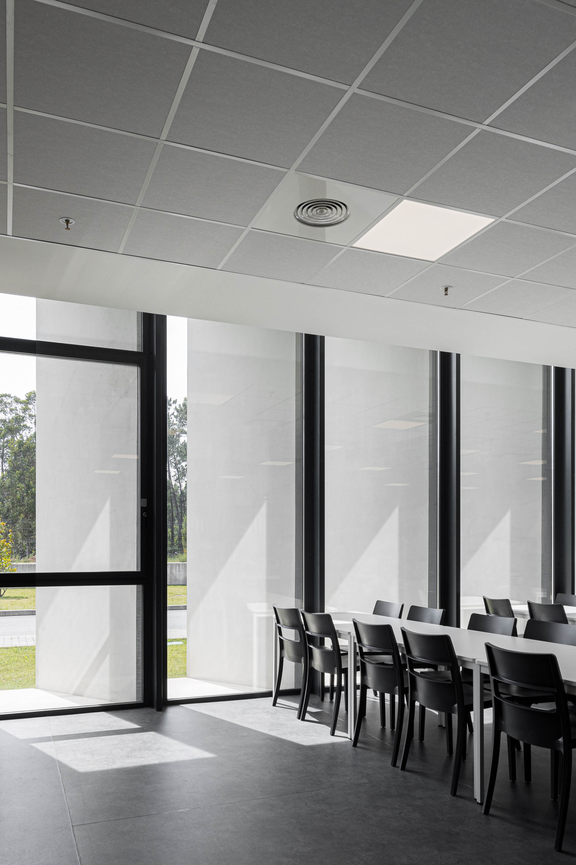 Sala de reuniões: Sala com mesa comprida, cadeiras pretas e janelas amplas com cortinas. — BW II – Edifício Industrial em Viana do Castelo arquitetura Multiprojectus em Viana do Castelo