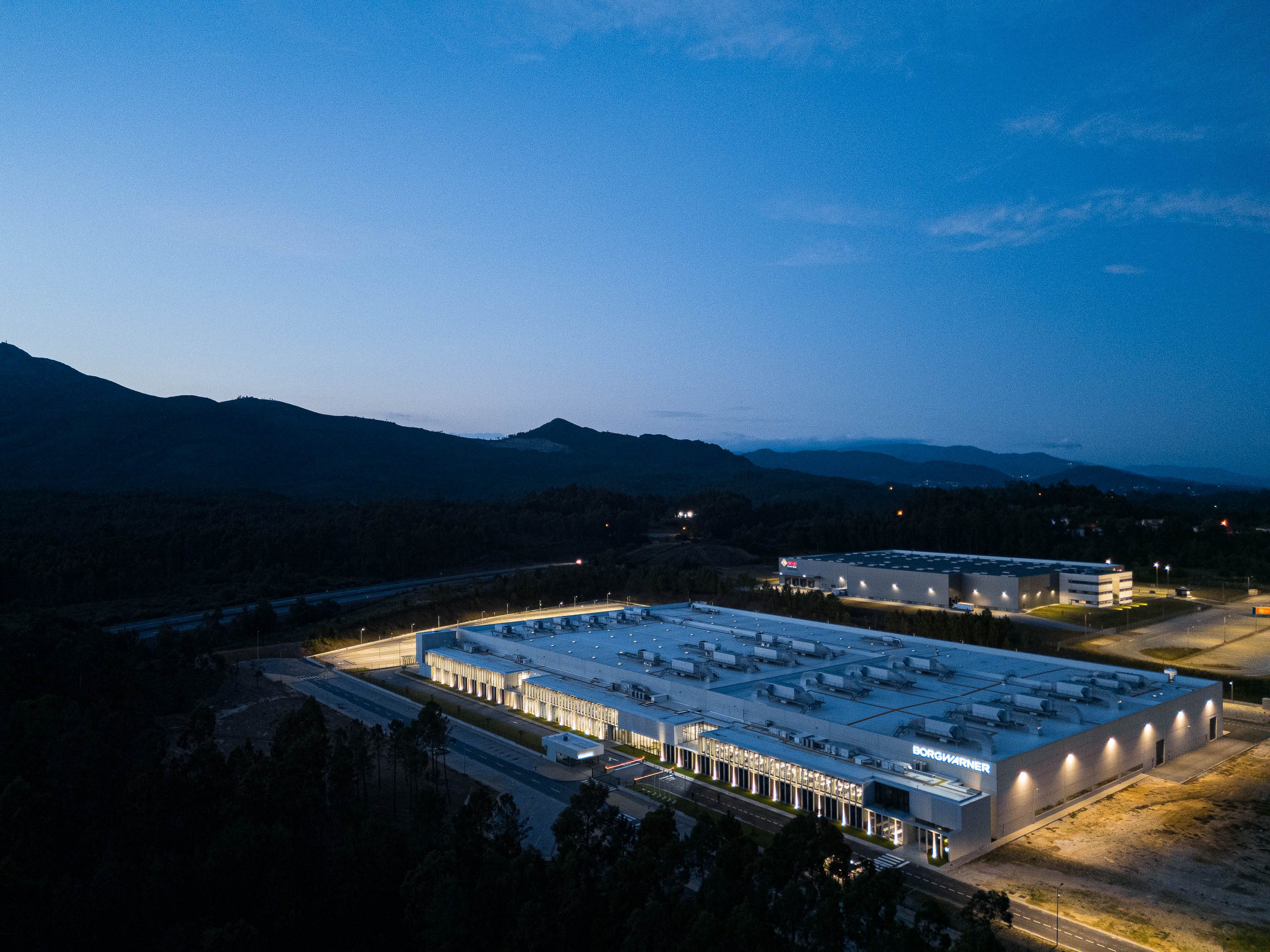 Exterior: Edifício industrial com colunas de betão e janelas iluminadas à noite. — BW II – Edifício Industrial em Viana do Castelo arquitetura Multiprojectus em Viana do Castelo