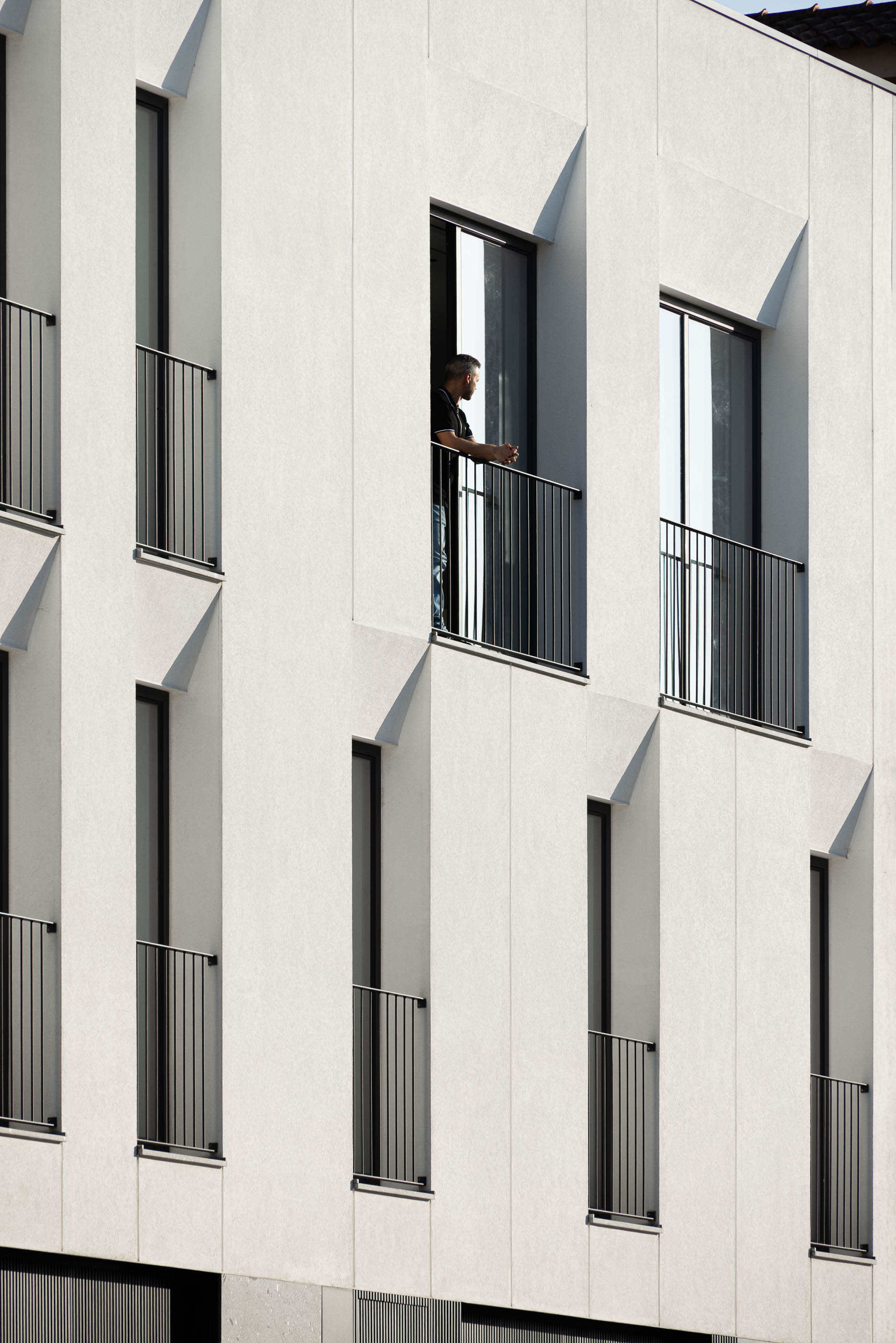 Fachada: Detalhe da fachada branca com varandas de metal preto e janelas verticais. — Casa SA arquitetura Sandro Ferreira Arquitectura em Braga