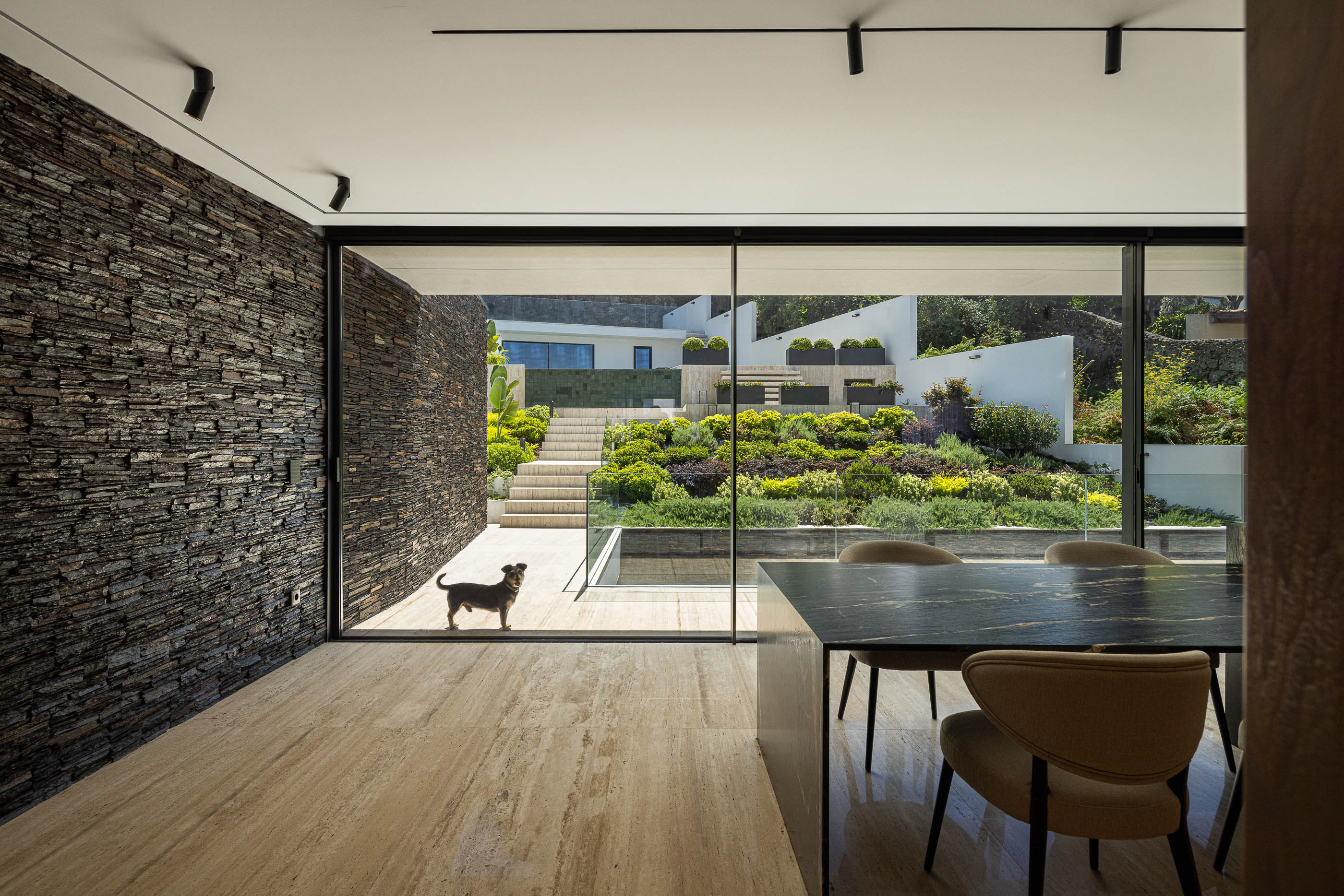 Sala de estar/jantar: Ilha de cozinha com vista para o jardim e parede em pedra. — Casa SA arquitetura Sandro Ferreira Arquitectura em Braga