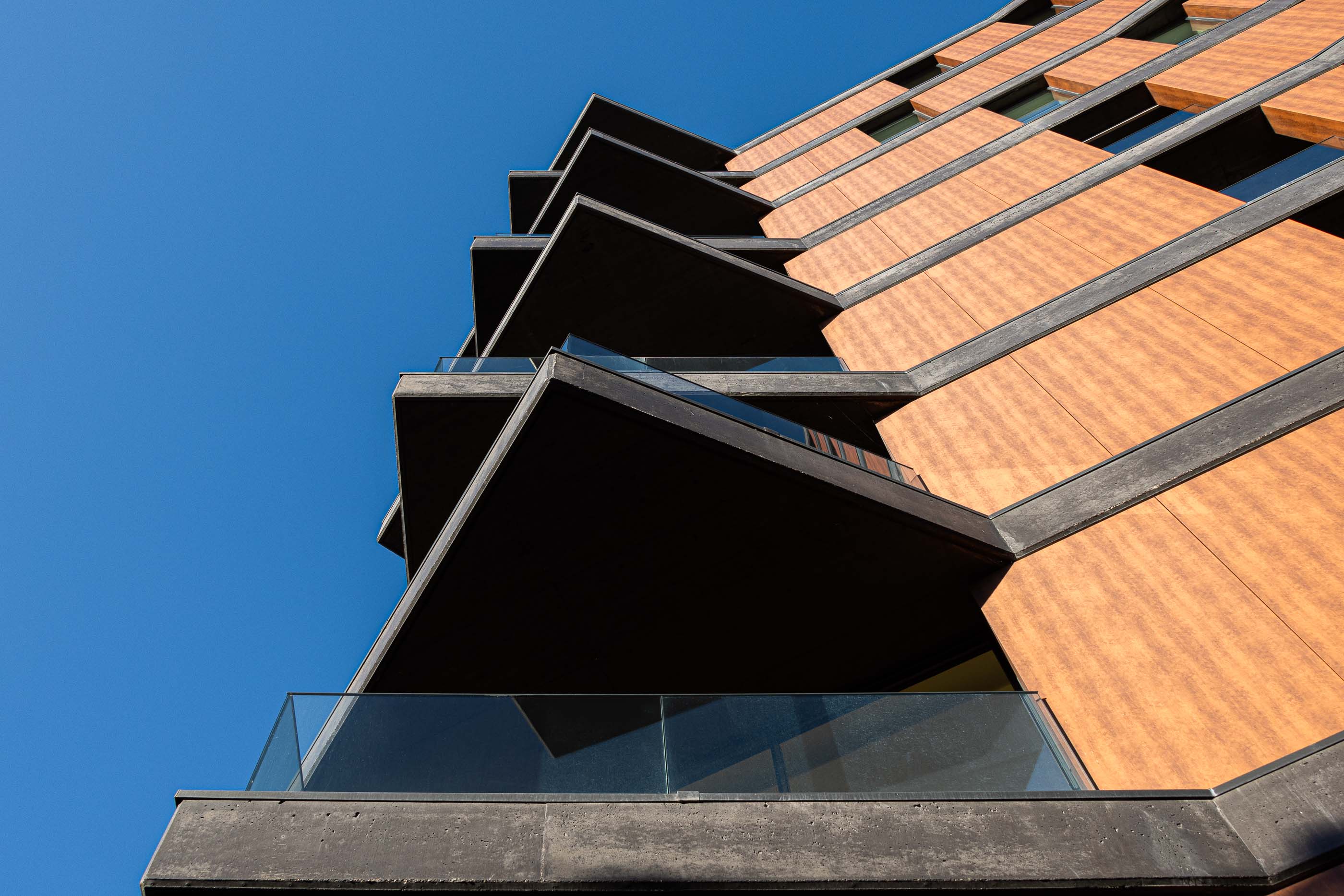 Fachada: Detalhe angular das varandas em betão e vidro da torre, com revestimento exterior em painéis cor de madeira. — Puro Tower arquitetura Mário Alves Arquitecto em Aveiro