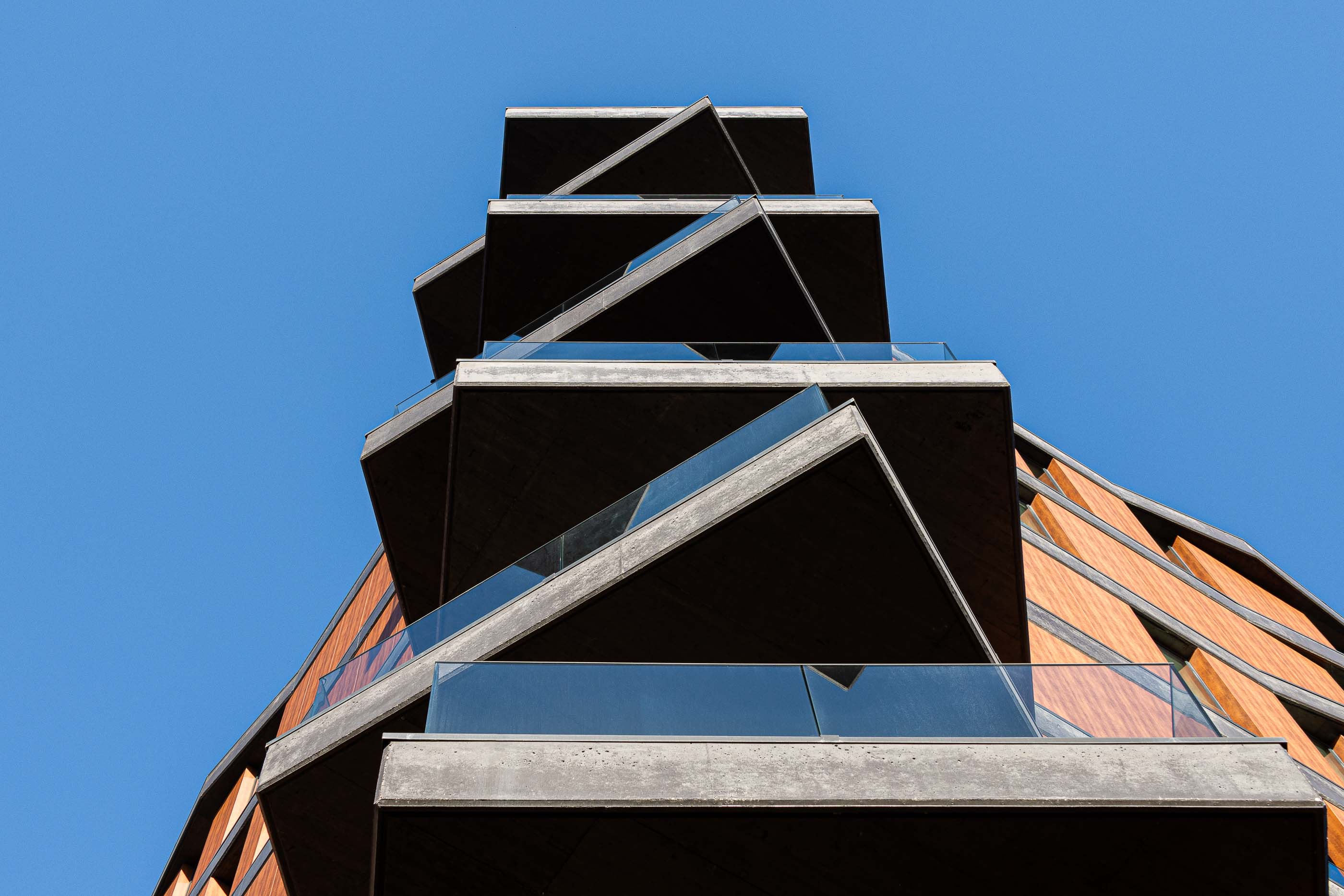 Fachada: Perspectiva ascendente das varandas triangulares em betão e vidro, com o céu azul como fundo. — Puro Tower arquitetura Mário Alves Arquitecto em Aveiro