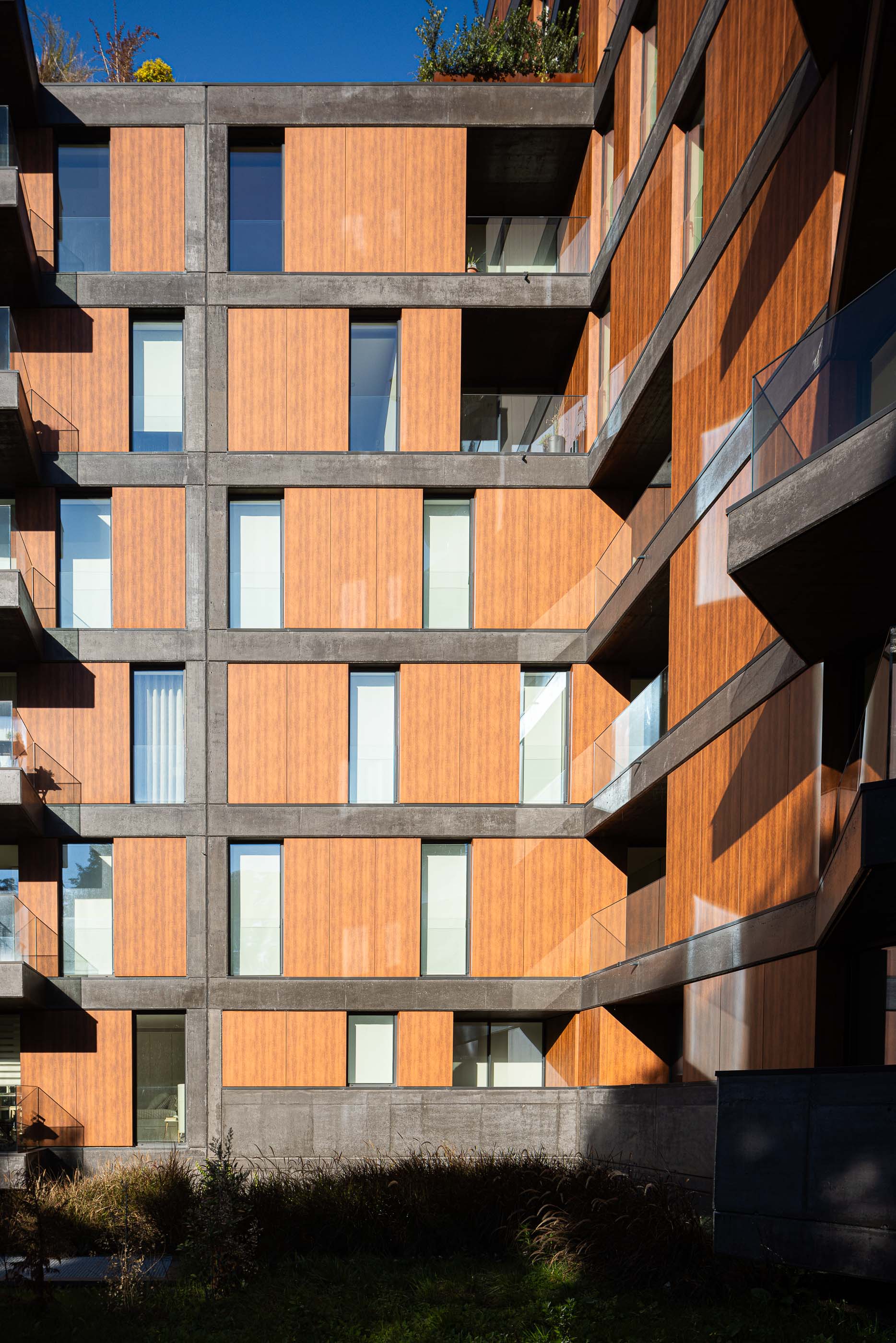 Fachada: Vista angular da fachada com revestimento em painéis de madeira e varandas em betão com guardas de vidro. — Puro Tower arquitetura Mário Alves Arquitecto em Aveiro