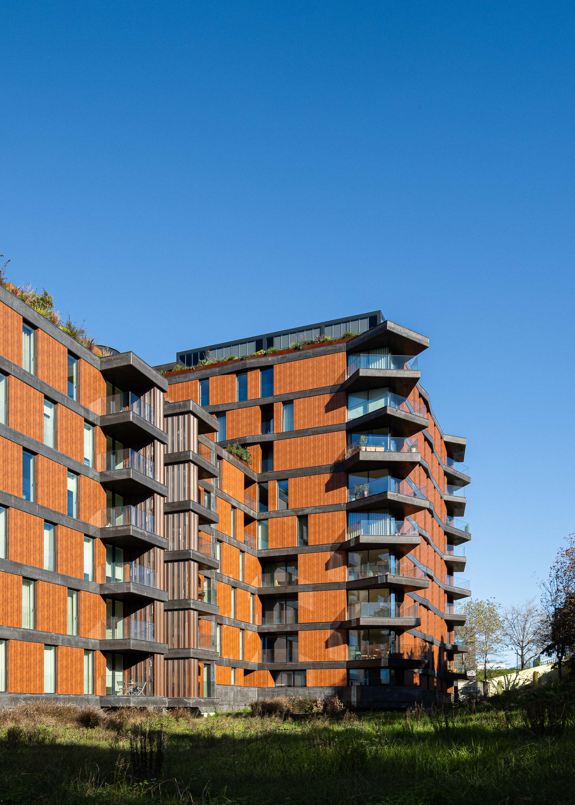 Fachada: Perspectiva lateral da torre com varandas em betão, revestimento em madeira e vegetação no topo. — Puro Tower arquitetura Mário Alves Arquitecto em Aveiro