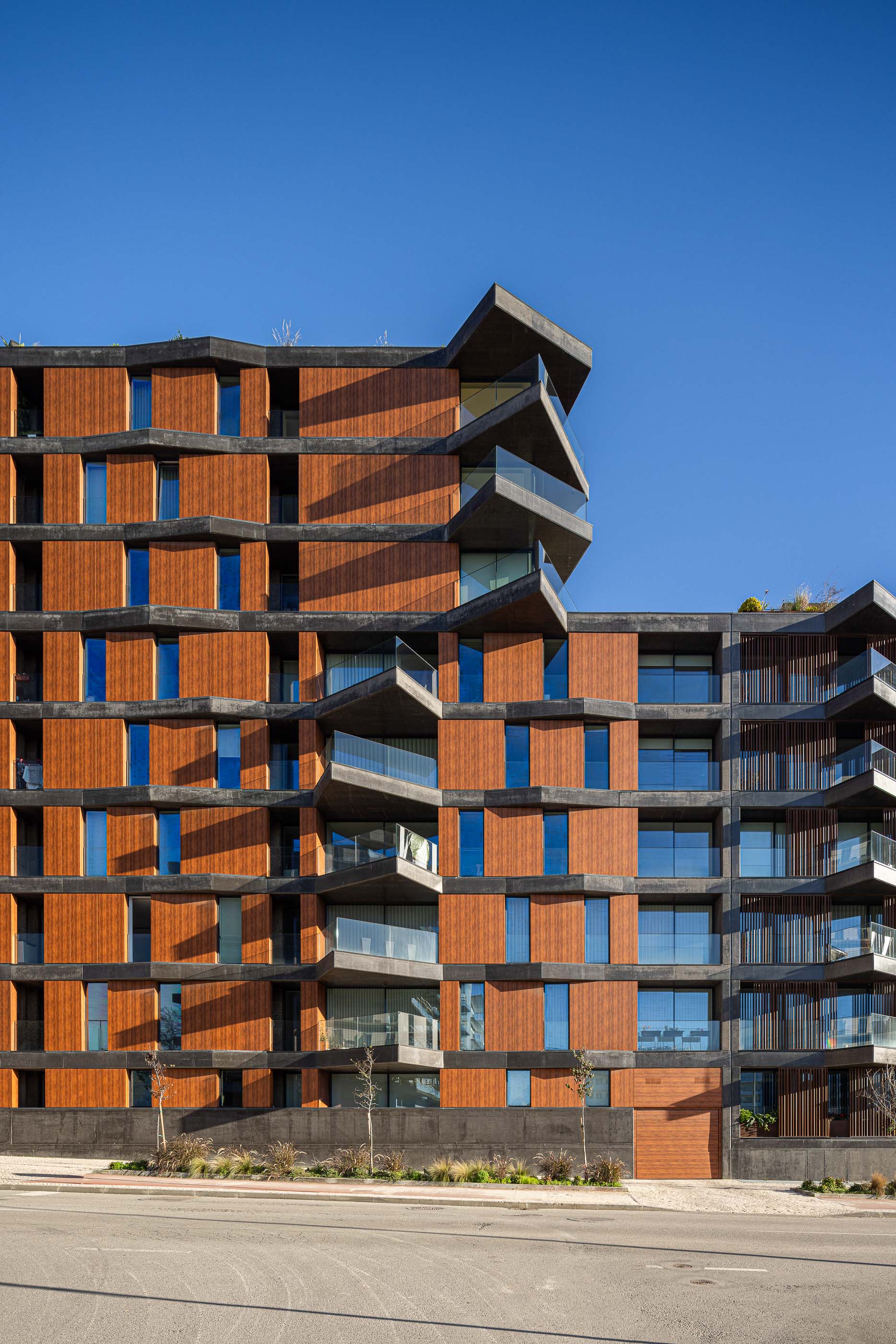 Fachada: Vista frontal da torre com varandas triangulares em betão e revestimento em madeira. — Puro Tower arquitetura Mário Alves Arquitecto em Aveiro