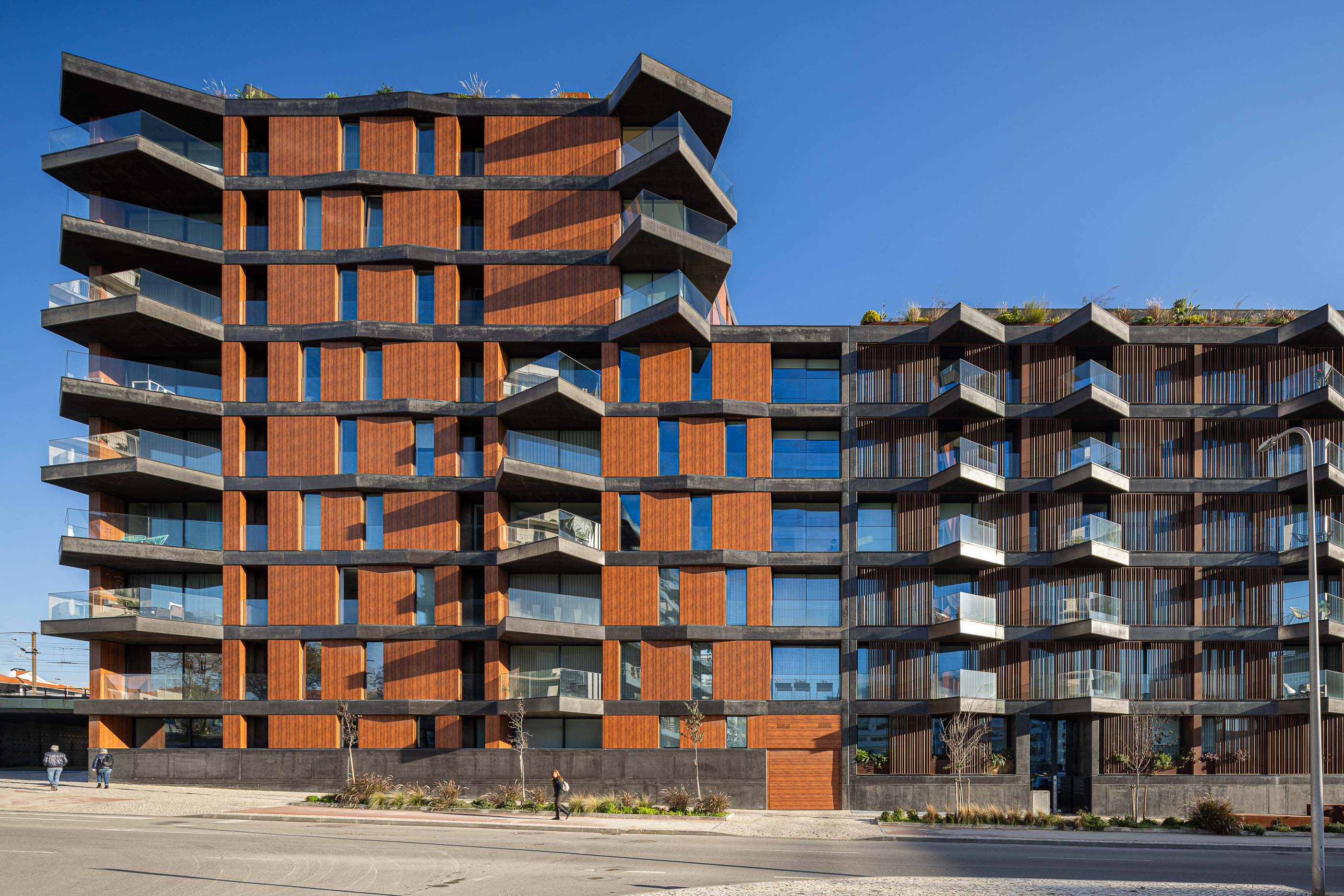 Fachada: Vista lateral da torre residencial com varandas e revestimento em madeira, com vegetação no topo. — Puro Tower arquitetura Mário Alves Arquitecto em Aveiro