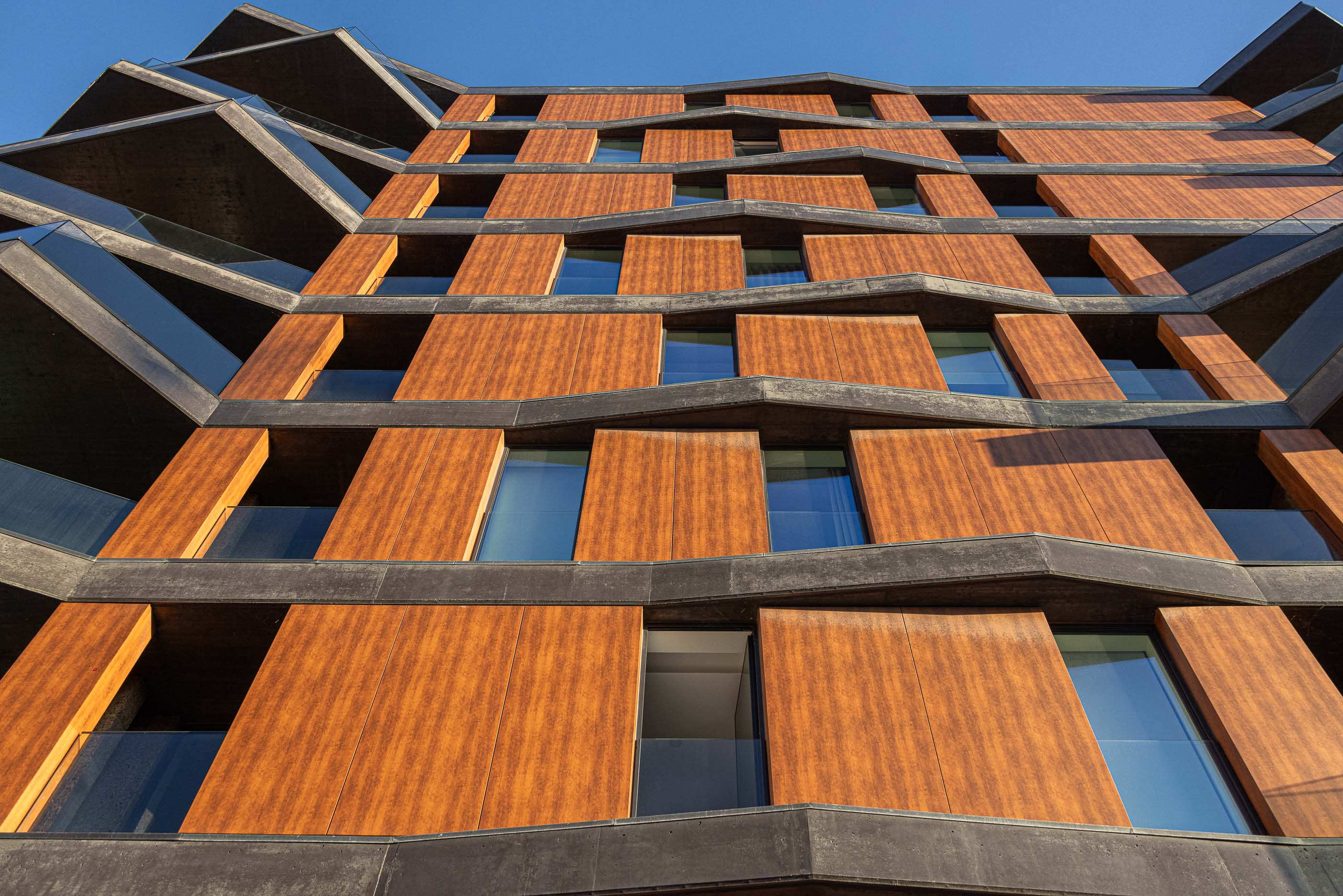 Fachada: Perspectiva ascendente da fachada com varandas em betão e revestimento em madeira. — Puro Tower arquitetura Mário Alves Arquitecto em Aveiro