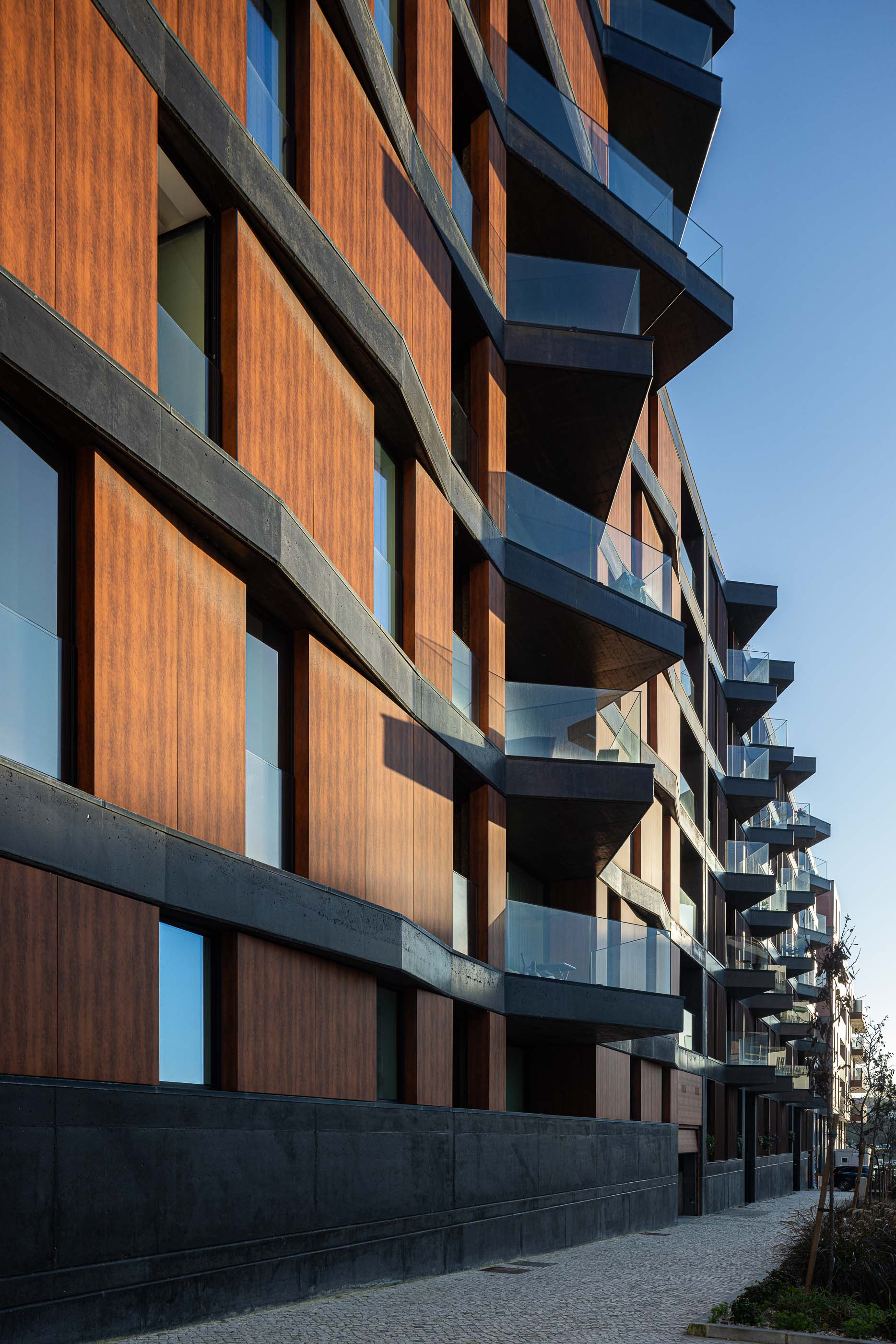 Fachada: Vista lateral da torre com varandas em betão e revestimento em madeira, junto ao passeio. — Puro Tower arquitetura Mário Alves Arquitecto em Aveiro