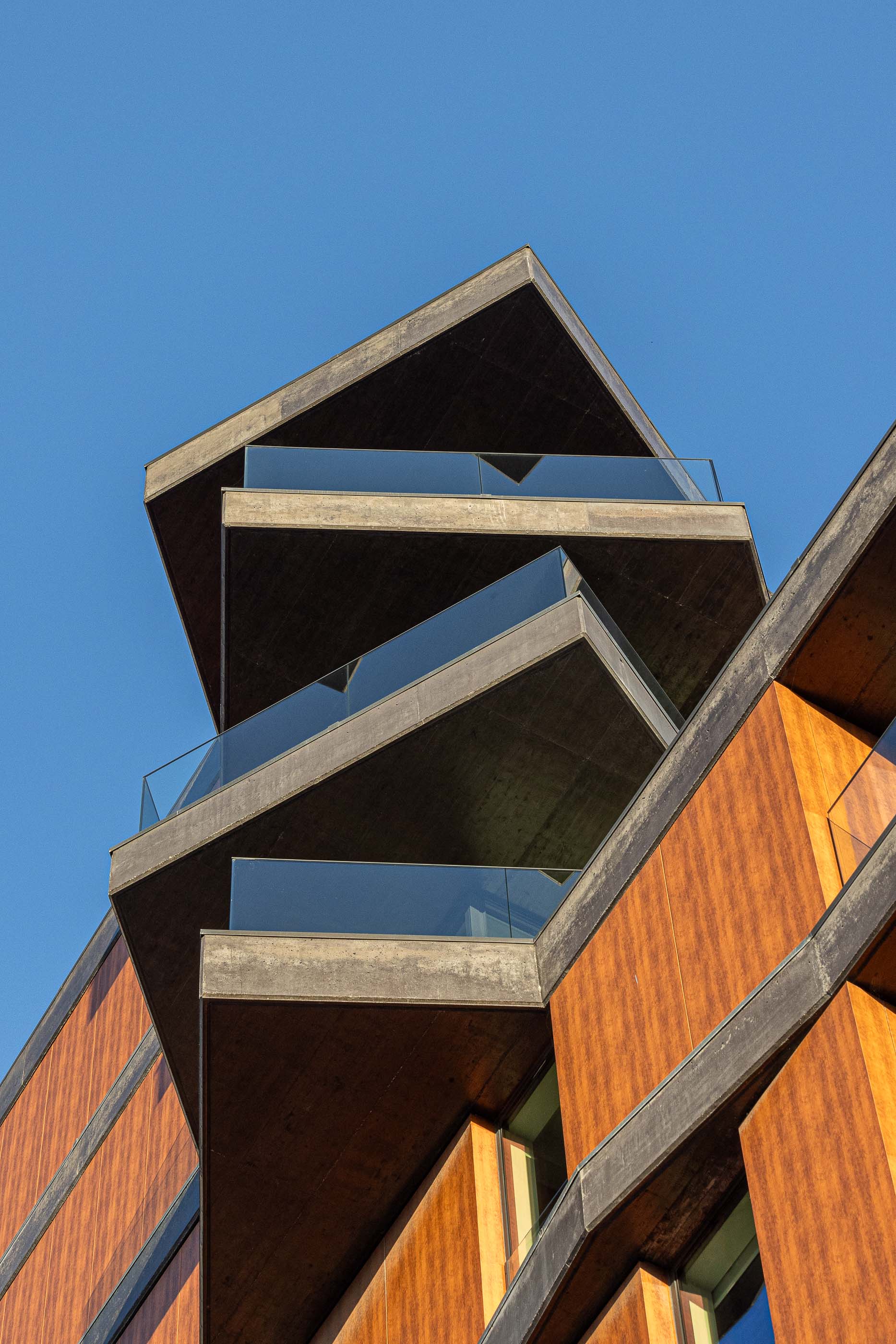 Fachada: Detalhe das varandas triangulares em betão com guardas de vidro, com revestimento exterior em madeira. — Puro Tower arquitetura Mário Alves Arquitecto em Aveiro