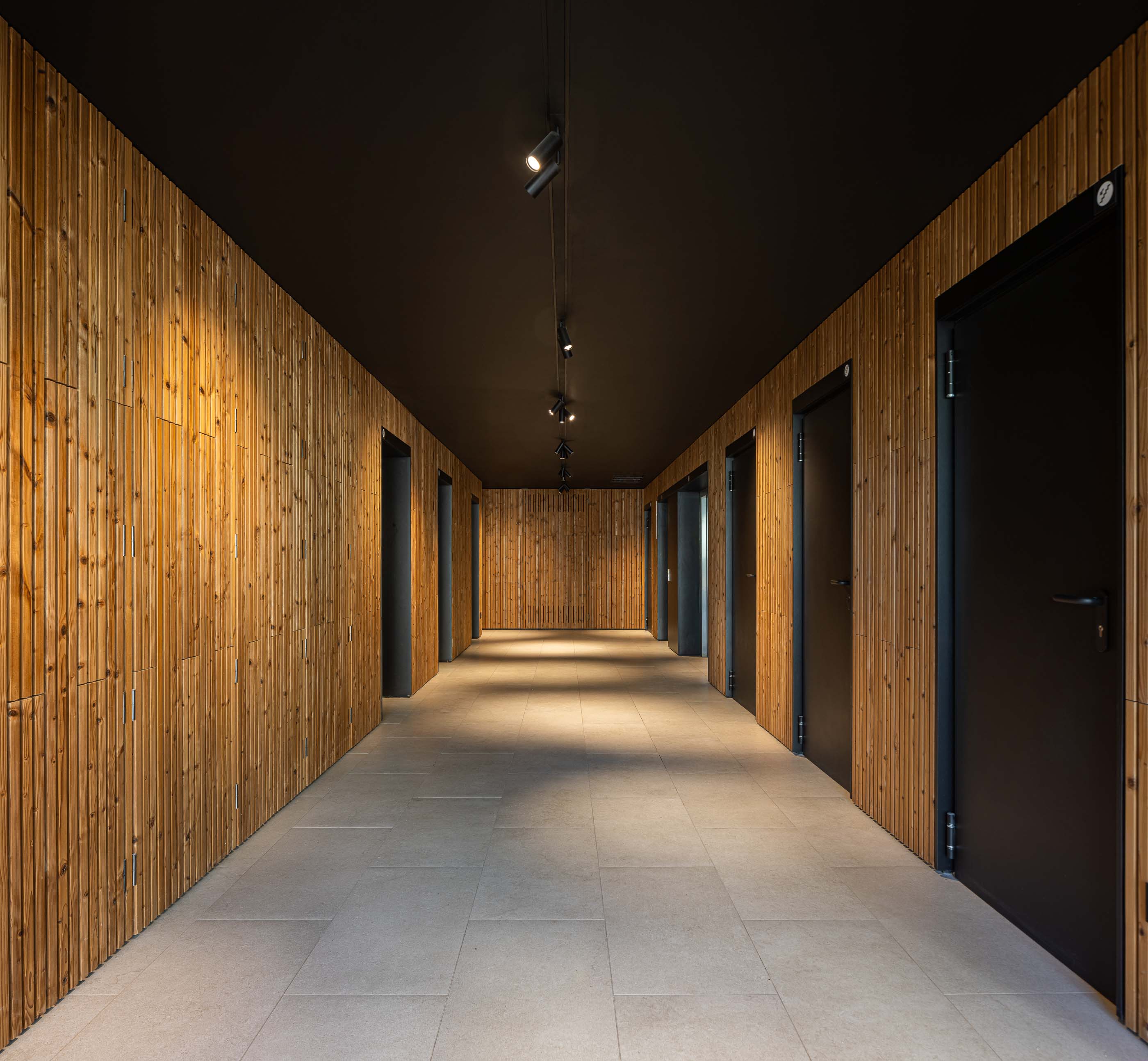 Corredor: Corredor com paredes revestidas a madeira, teto preto e pavimento cerâmico cinzento. Candeeiros suspensos. — Puro Tower arquitetura Mário Alves Arquitecto em Aveiro