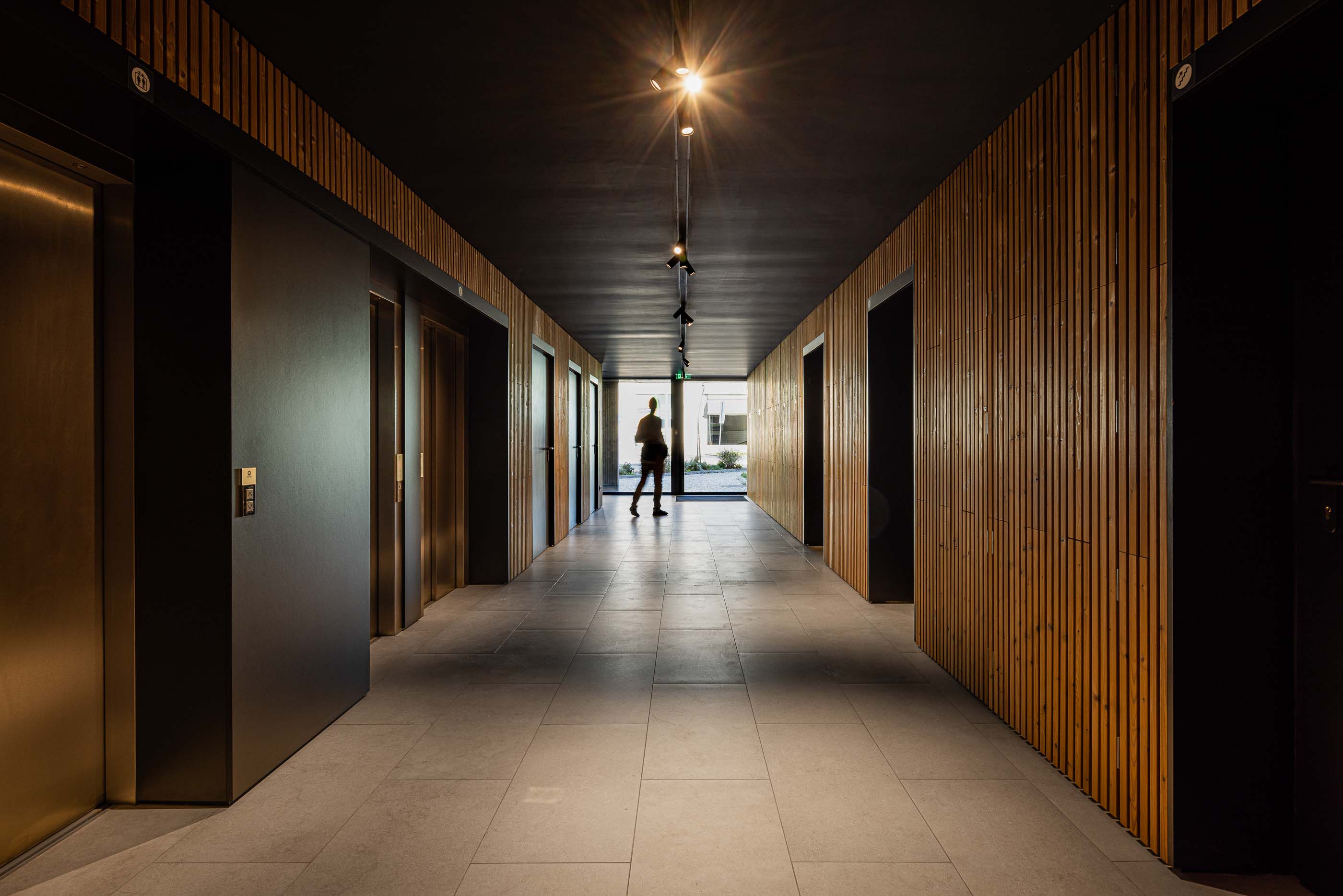 Corredor: Corredor com elevadores e portas de acesso aos apartamentos, paredes em madeira e pavimento cerâmico. — Puro Tower arquitetura Mário Alves Arquitecto em Aveiro