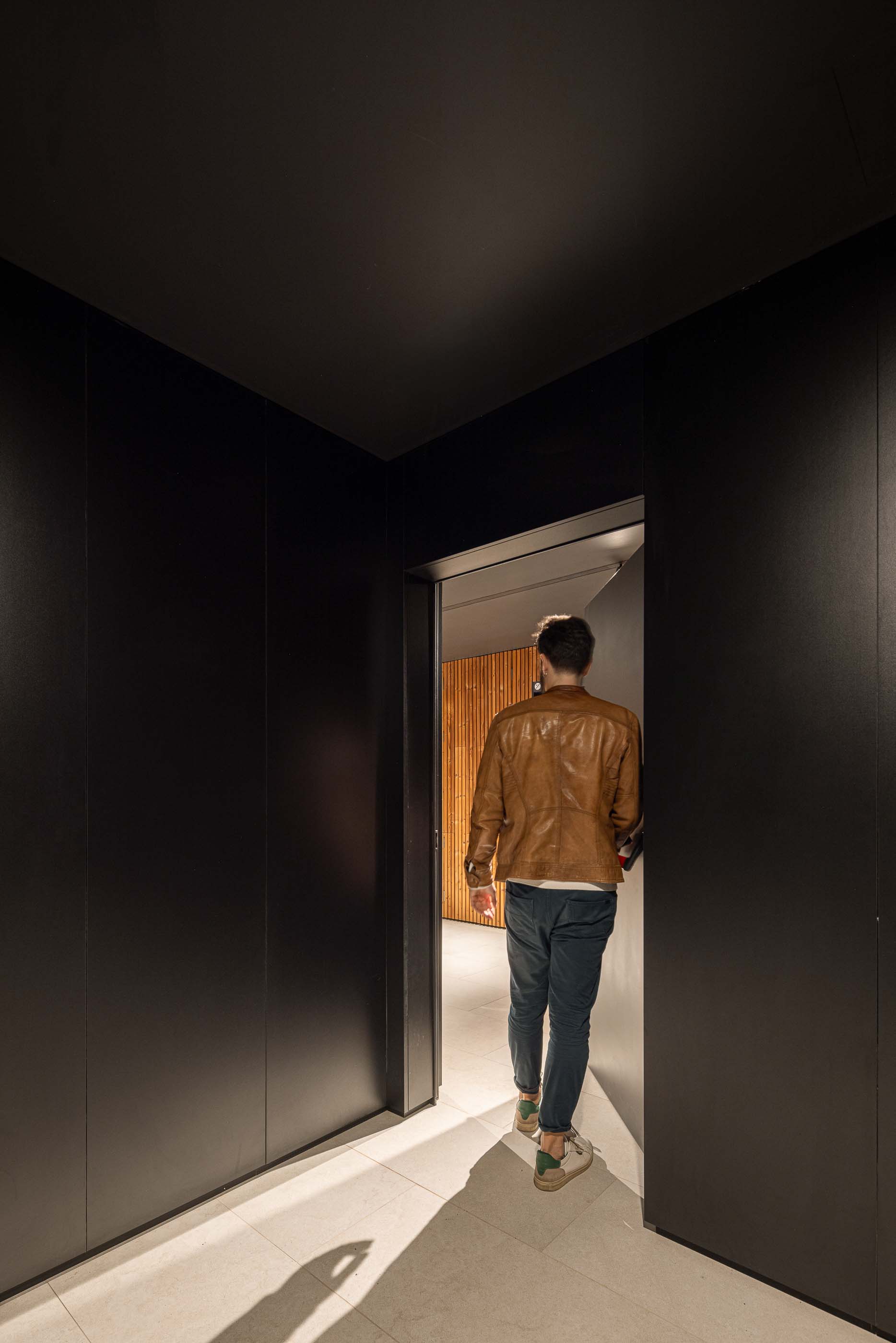 Corredor: Homem a entrar num apartamento, com paredes pretas e pavimento cerâmico claro. — Puro Tower arquitetura Mário Alves Arquitecto em Aveiro