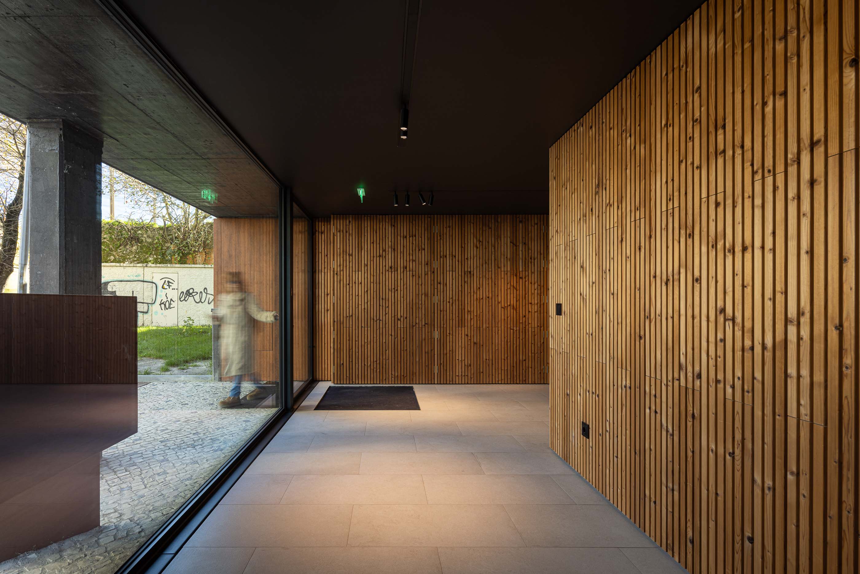 Hall de entrada: Hall com paredes revestidas a madeira, pavimento cerâmico e grandes janelas envidraçadas. — Puro Tower arquitetura Mário Alves Arquitecto em Aveiro