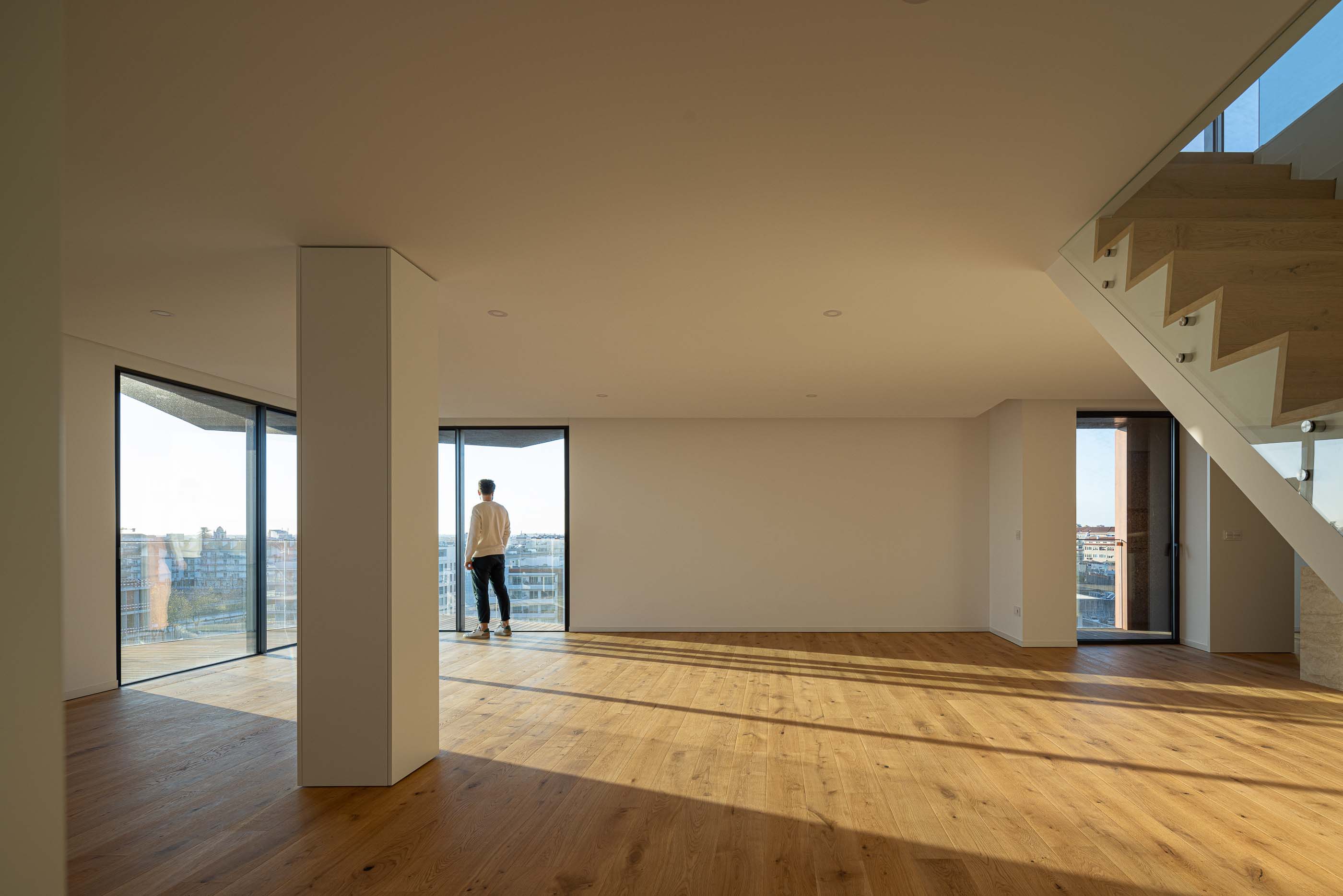 Sala de estar: Sala ampla com pavimento em madeira, paredes brancas e grandes janelas com vista para a cidade. — Puro Tower arquitetura Mário Alves Arquitecto em Aveiro