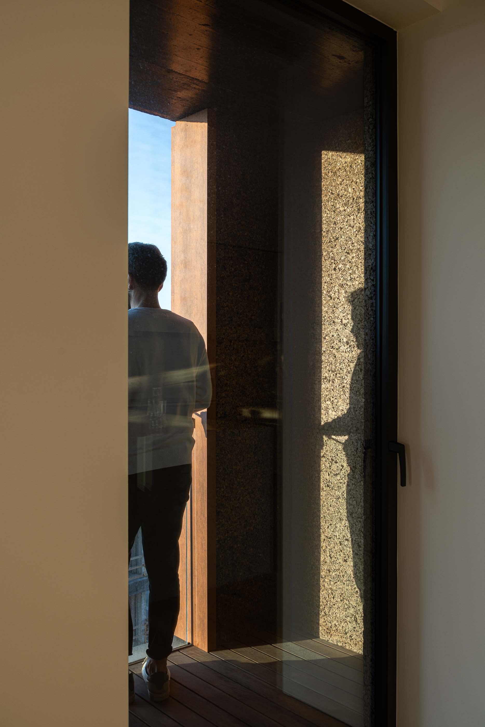 Varanda: Homem a olhar para o exterior numa varanda com pavimento em madeira e painéis de cortiça. — Puro Tower arquitetura Mário Alves Arquitecto em Aveiro