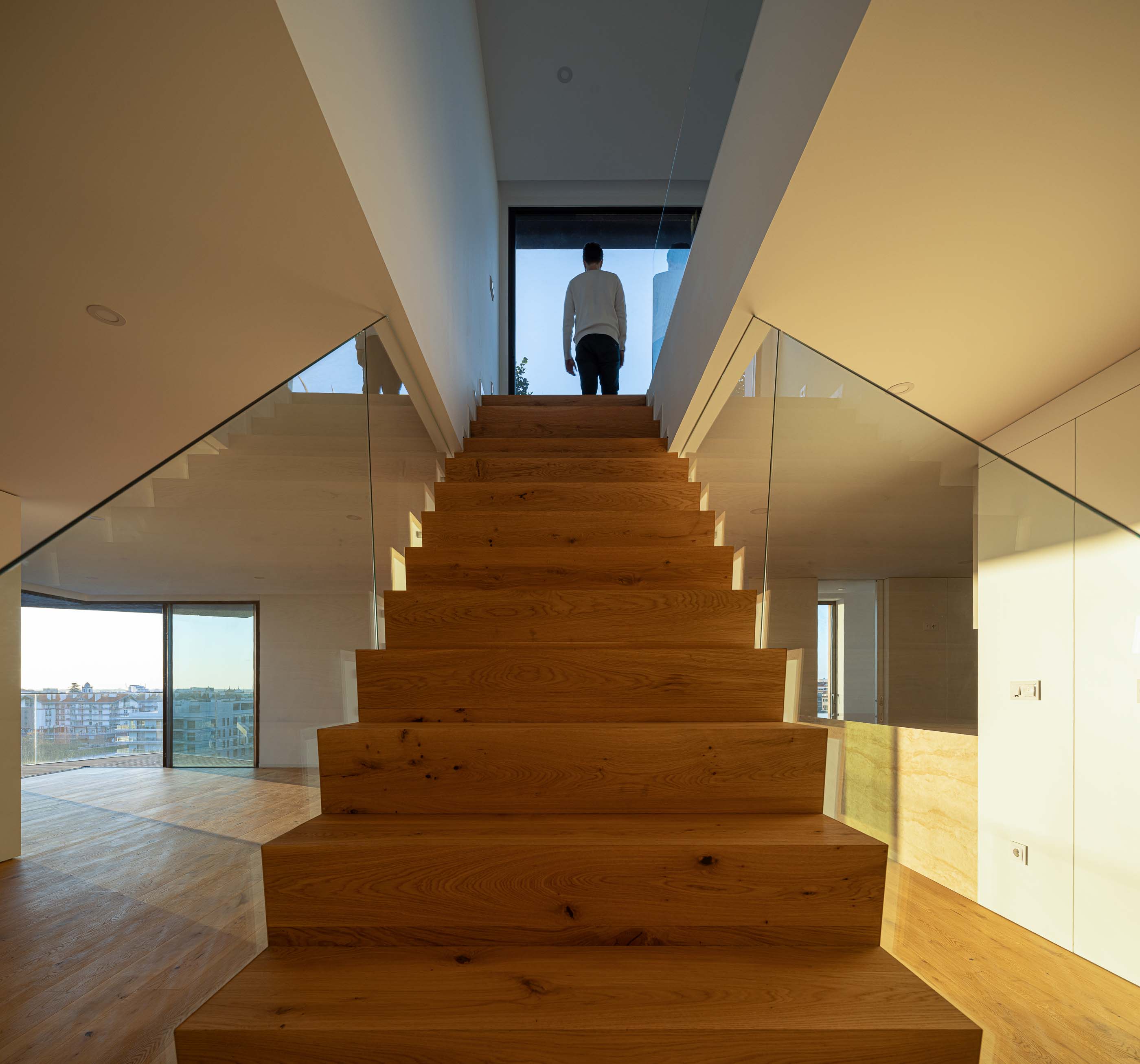 Escada: Escada em madeira com guardas de vidro, com vista para a sala de estar e para a cidade. — Puro Tower arquitetura Mário Alves Arquitecto em Aveiro