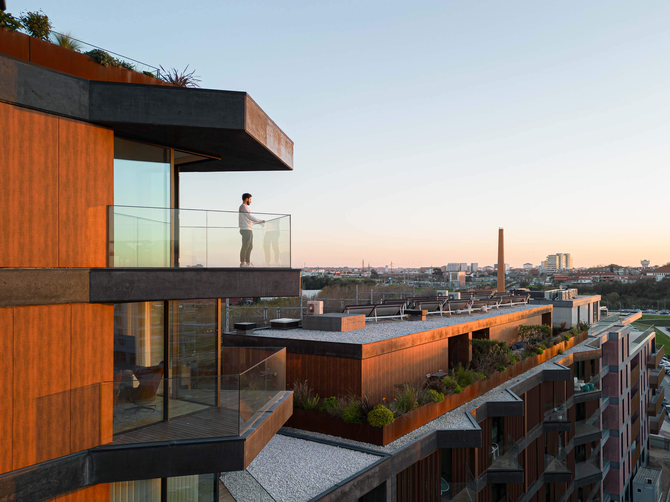 Varanda: Homem numa varanda com vista para a cidade, com revestimento em madeira e vegetação. — Puro Tower arquitetura Mário Alves Arquitecto em Aveiro