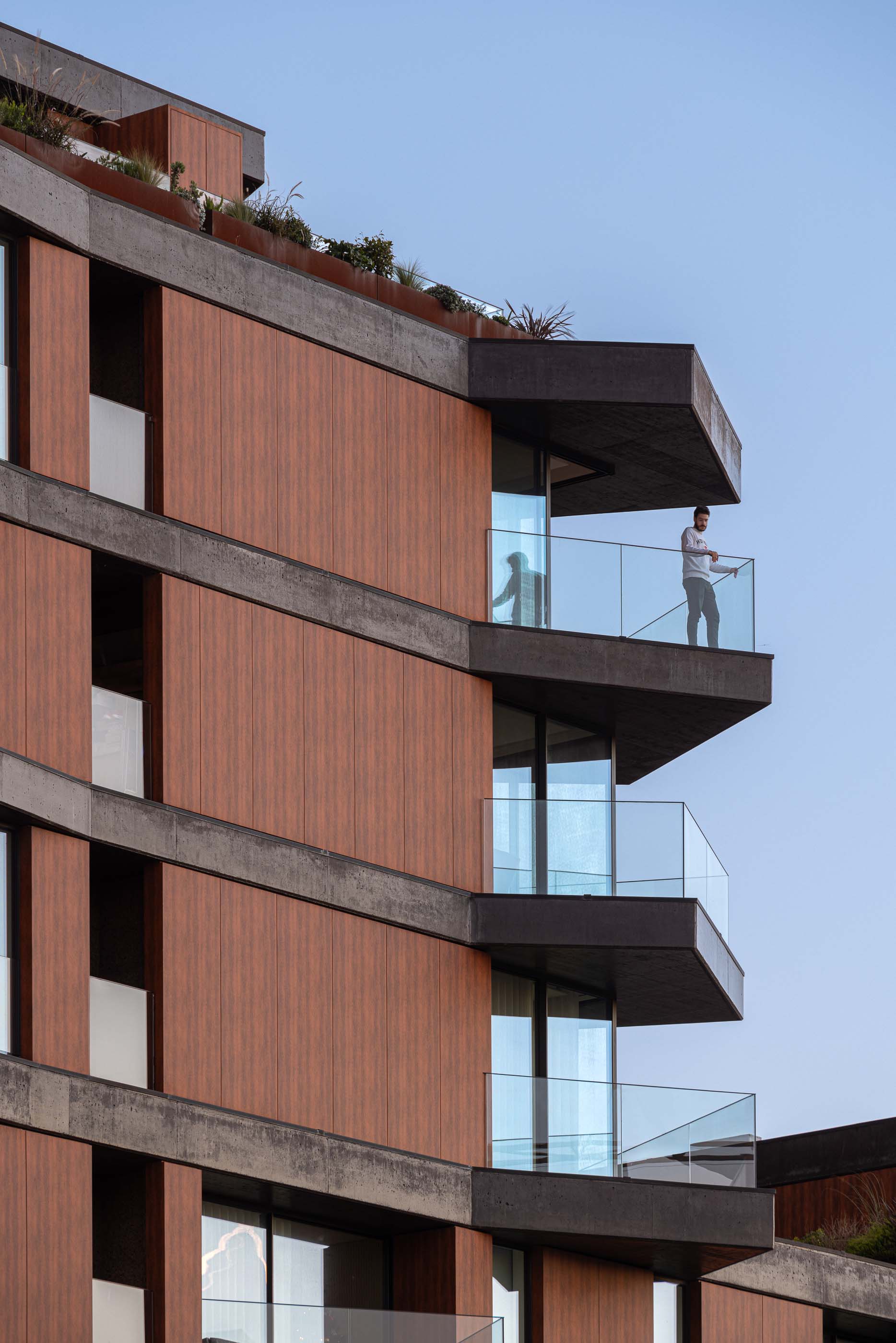 Varanda: Homem numa varanda com vista para a cidade, com revestimento em madeira e betão. — Puro Tower arquitetura Mário Alves Arquitecto em Aveiro
