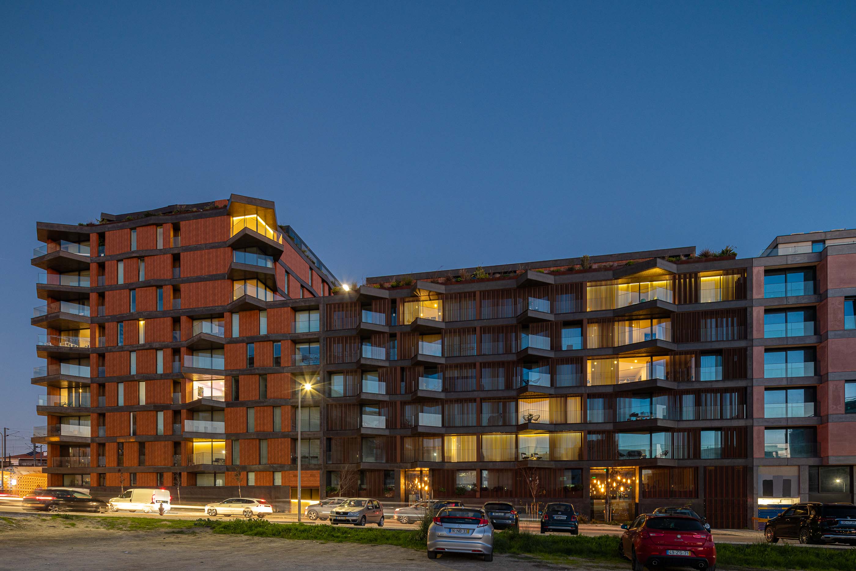 Exterior: Vista noturna da torre residencial com varandas iluminadas e estacionamento. — Puro Tower arquitetura Mário Alves Arquitecto em Aveiro