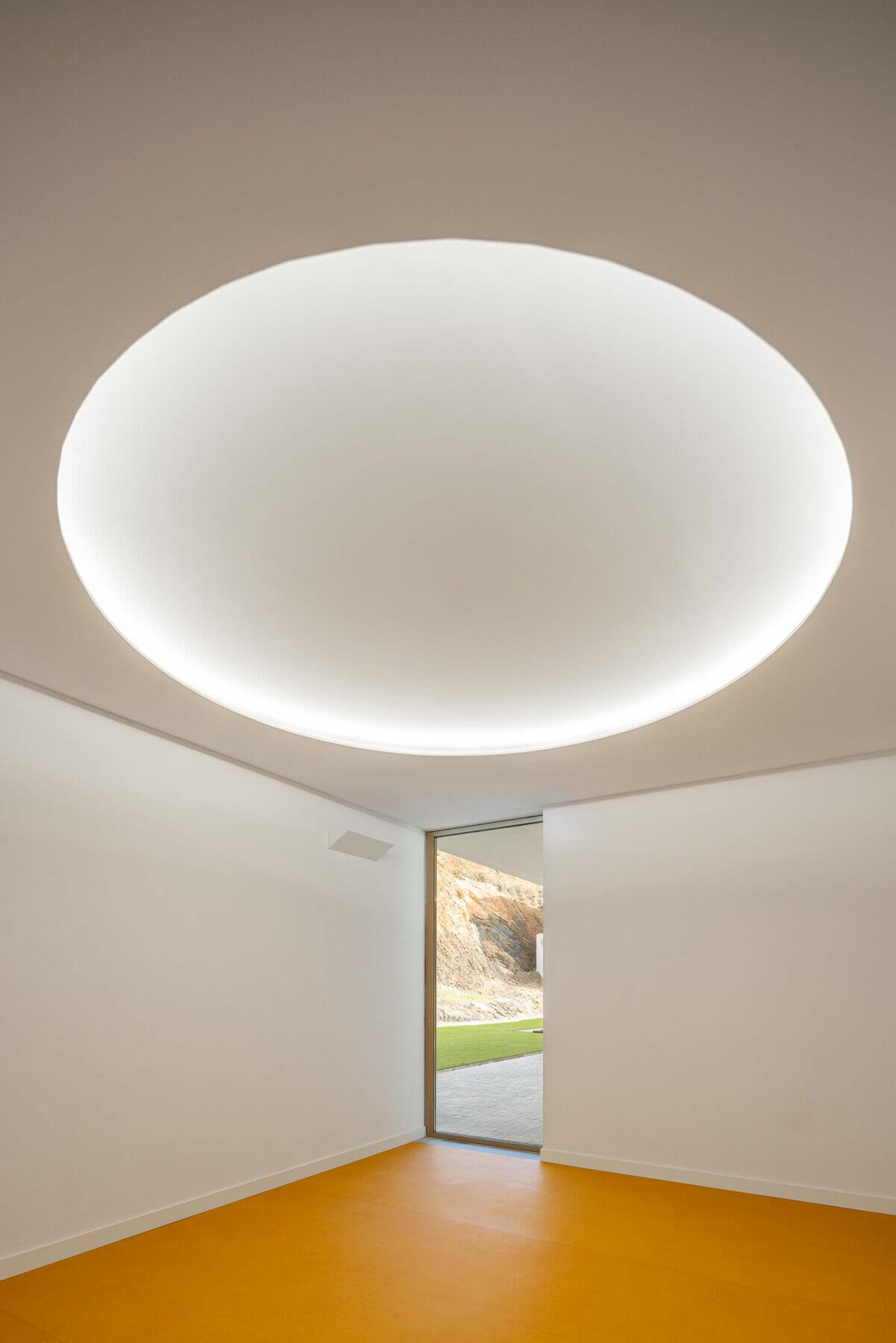 Sala sensorial: Candeeiro circular embutido no teto branco, pavimento amarelo e porta envidraçada para o exterior. — Associação Paralisia Cerebral de Odemira – APCO arquitetura Filipe Xavier Oliveira em Odemira