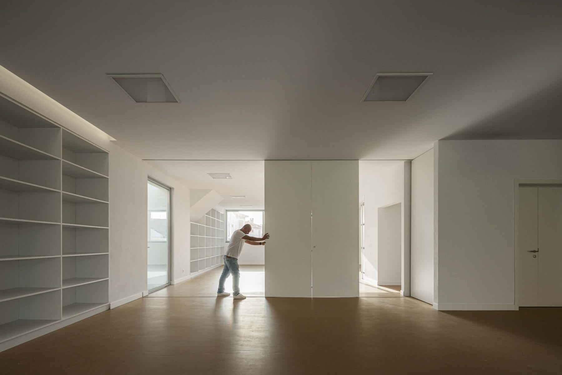 Sala polivalente: Espaço amplo com estantes brancas, pavimento castanho e portas deslizantes. — Associação Paralisia Cerebral de Odemira – APCO arquitetura Filipe Xavier Oliveira em Odemira